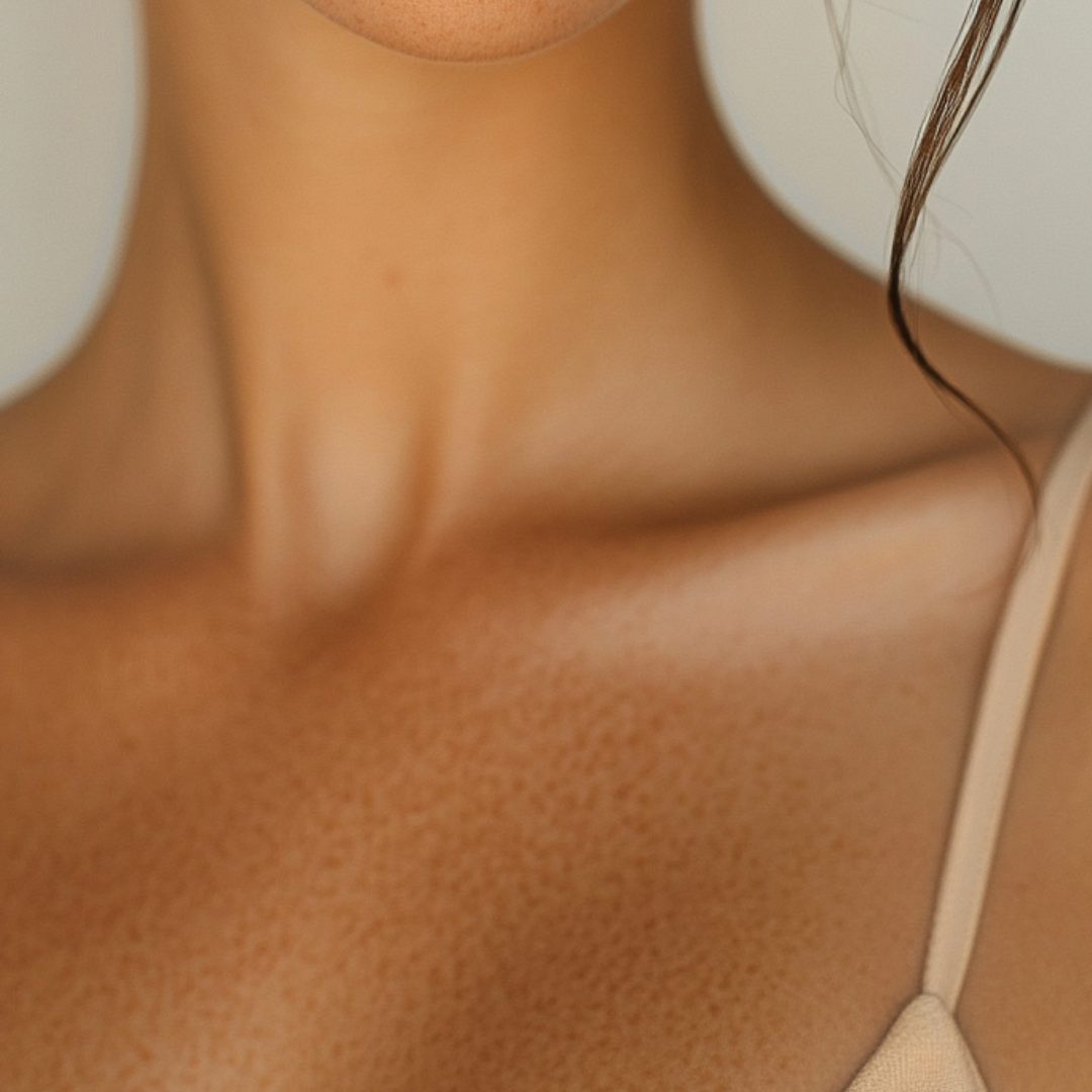 Close-up of a woman's neck, shoulder, and collarbone in a beige top, with a loose curl of hair on the right side