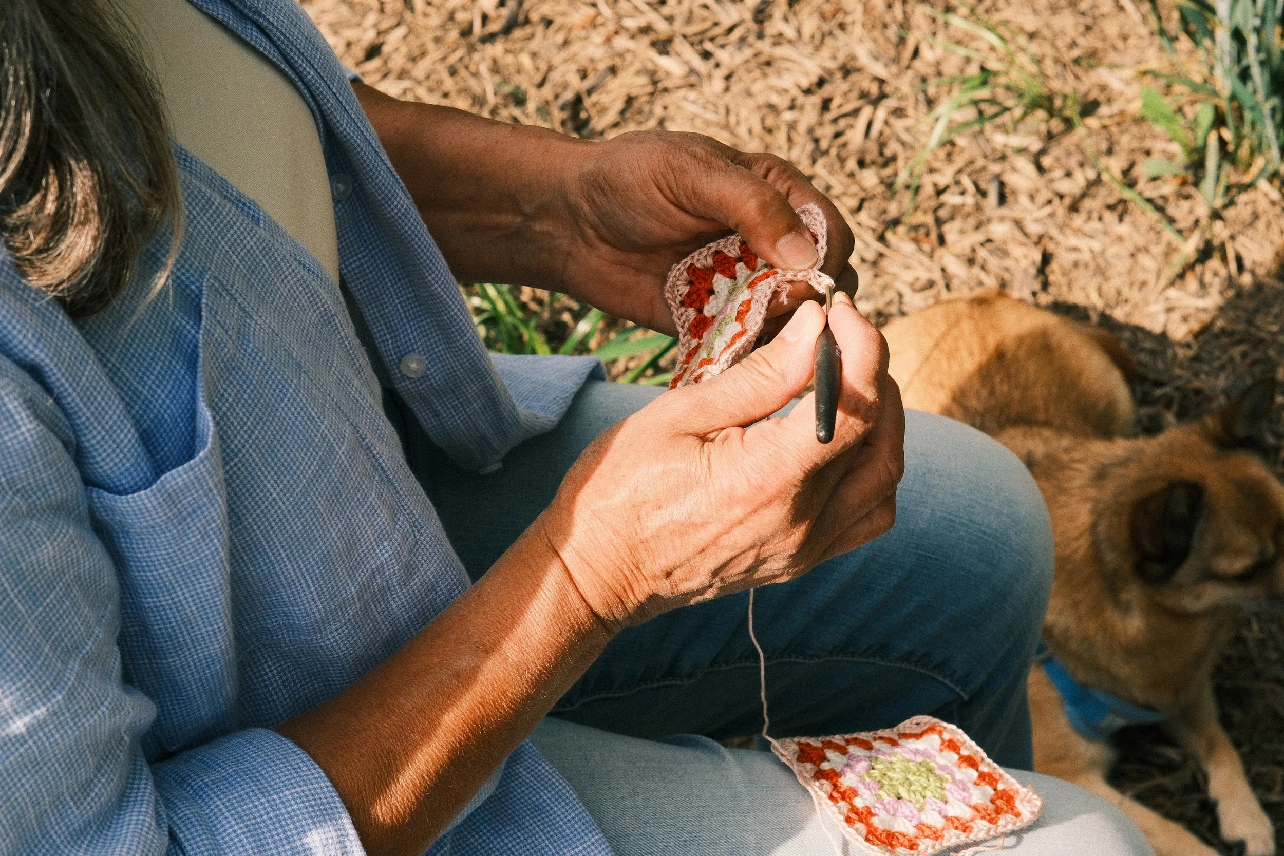 Personne en train de crocheter en plein air, avec un chien allongé à proximité.