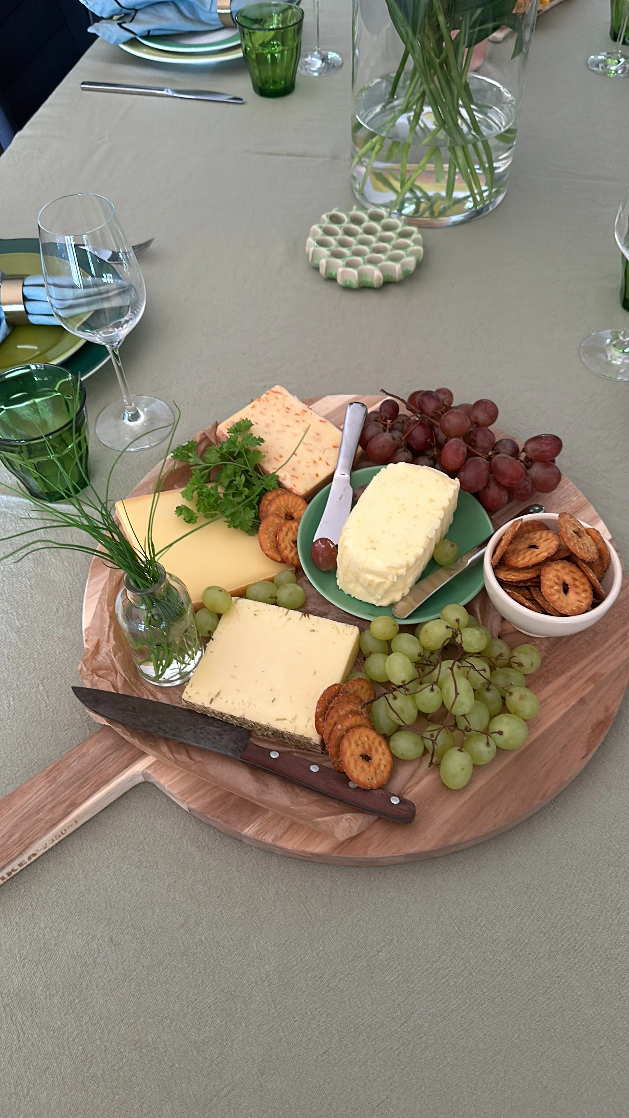 Käse, Trauben, Trockenfrüchte und Kekse auf einem Holzbrett, gedeckt mit einem grünen Tischdecken. Es ist ein Käsebuffet.