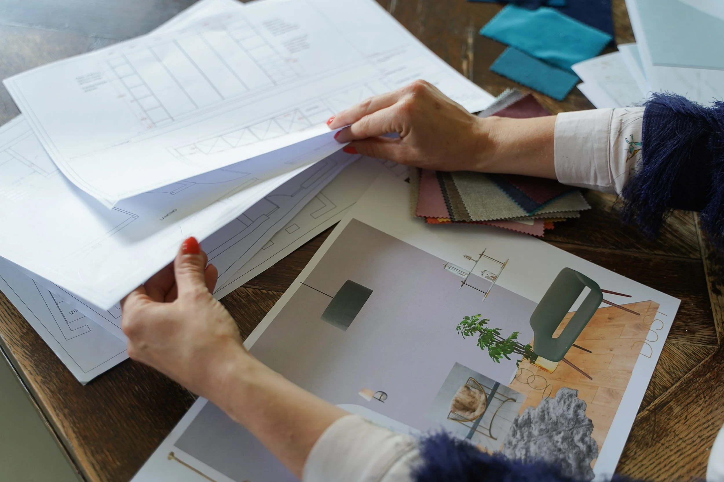 A person flipping through architectural blueprints and color samples on a wooden table.