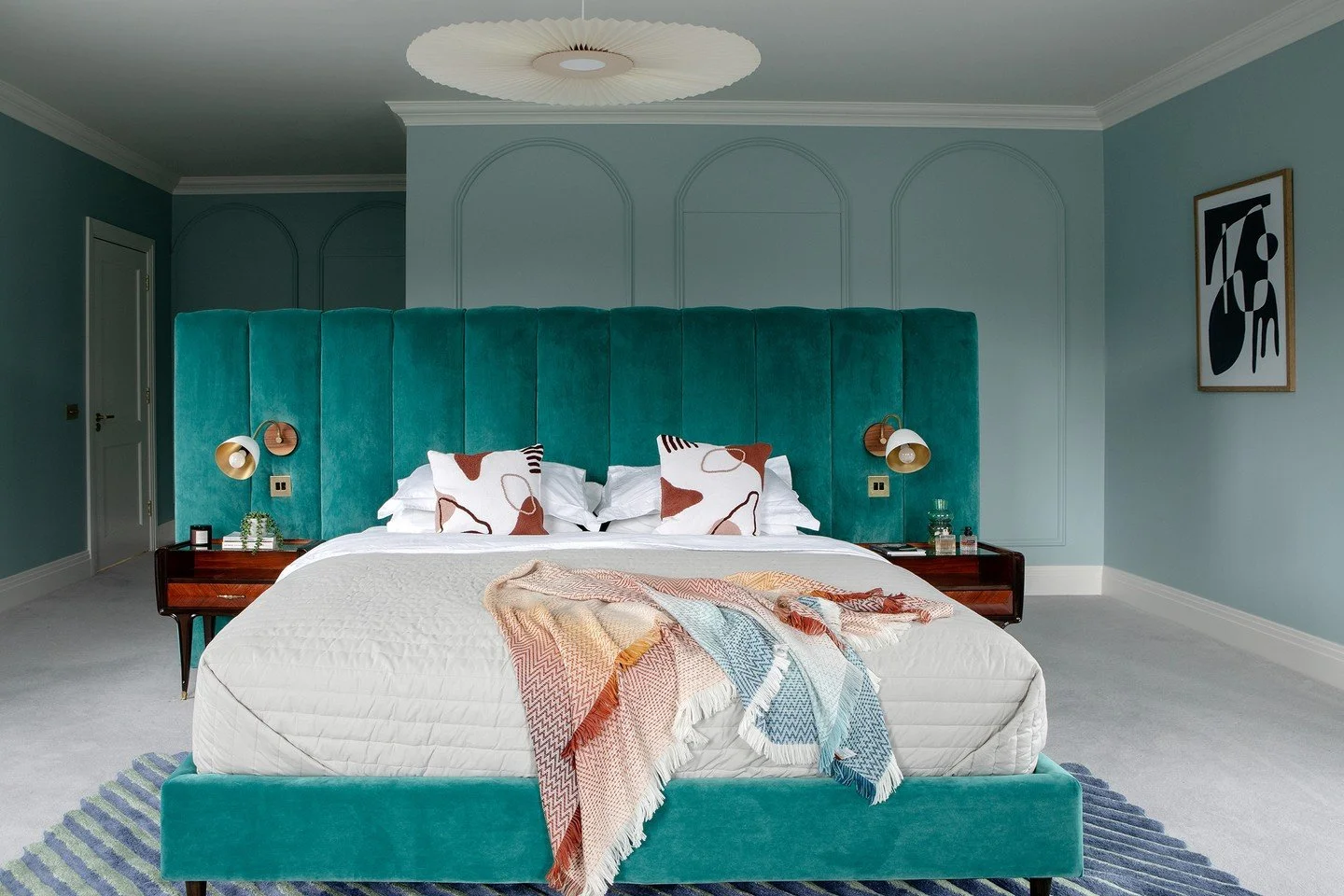 Not every element in a room should compete for attention.

Here, the oversized teal velvet headboard and matching bed are unapologetically bold. They set the tone for the space.
Around them, quieter details do the supporting work: tonal arch panellin