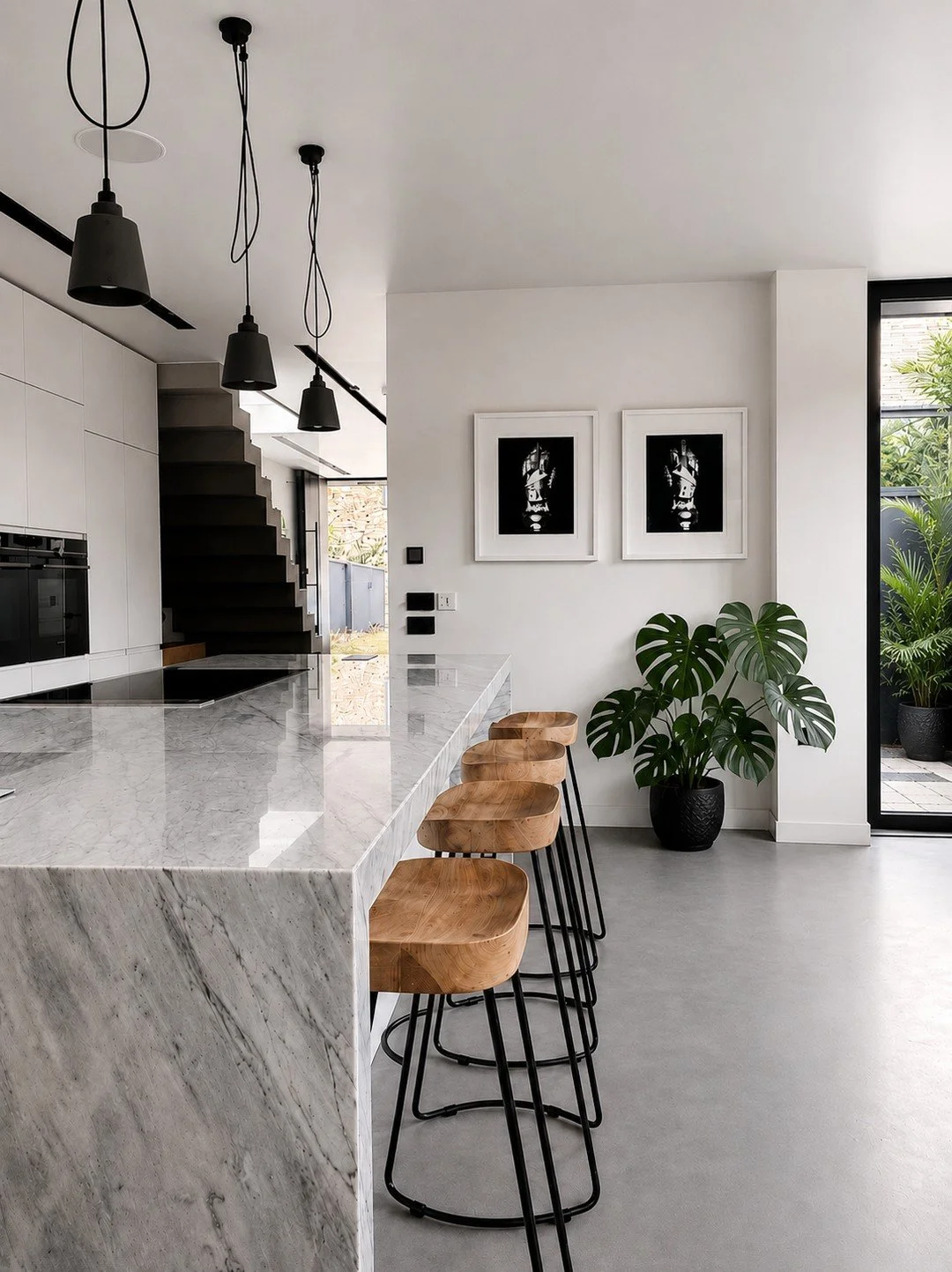 A monochrome colour scheme doesn't have to feel cold.⁠
⁠
The architectural palette here is restrained &mdash; white, black, grey and heavily veined marble.⁠
⁠
Against that, the warmth of the timber stools and the green in the planting become much mor