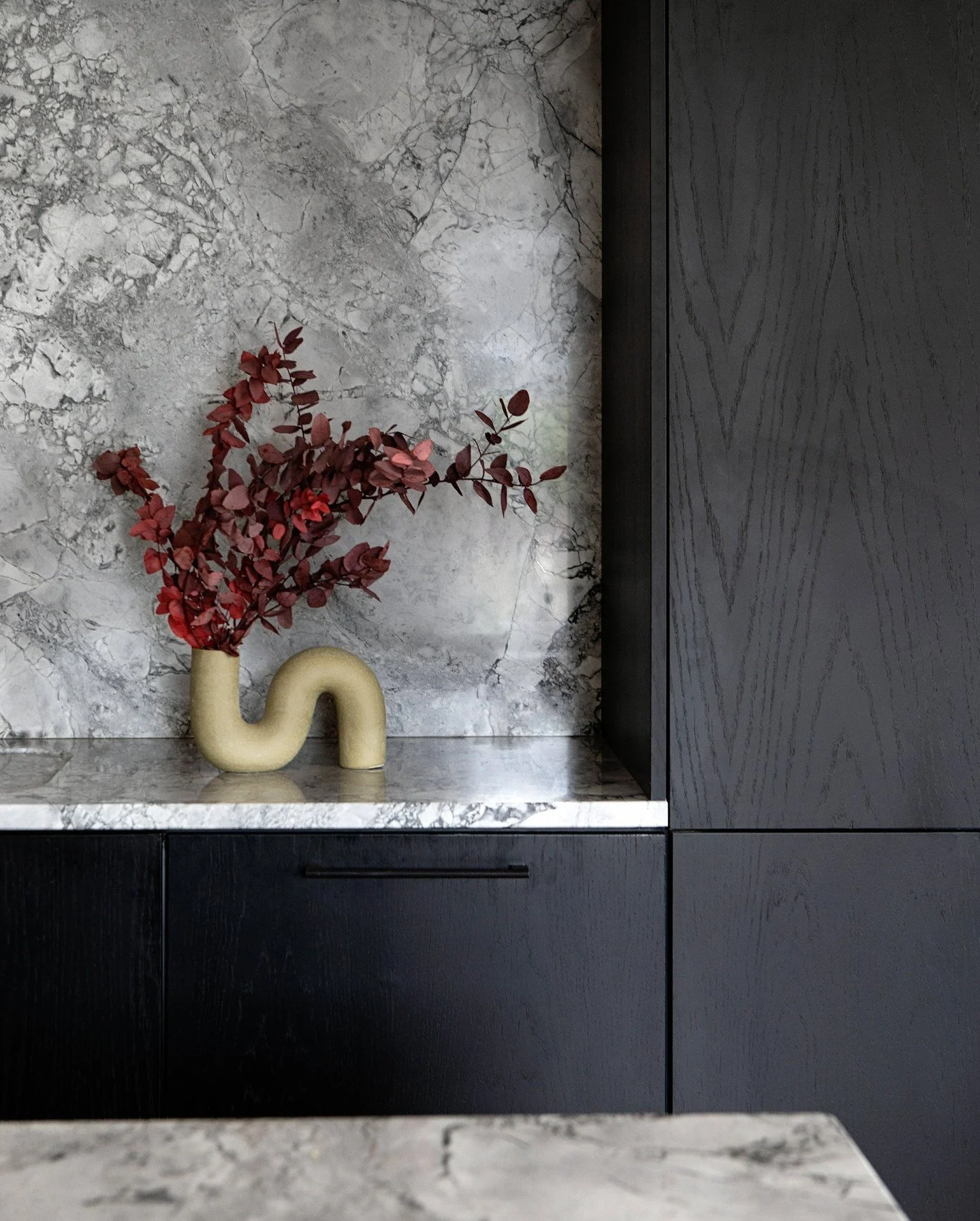 When the natural materials are this stunning, you don't need much to set them off.

Here, heavily veined stone and dark timber cabinetry do most of the work, so the styling can stay simple &mdash; just a sculptural vase and a few branches.

Coloured 