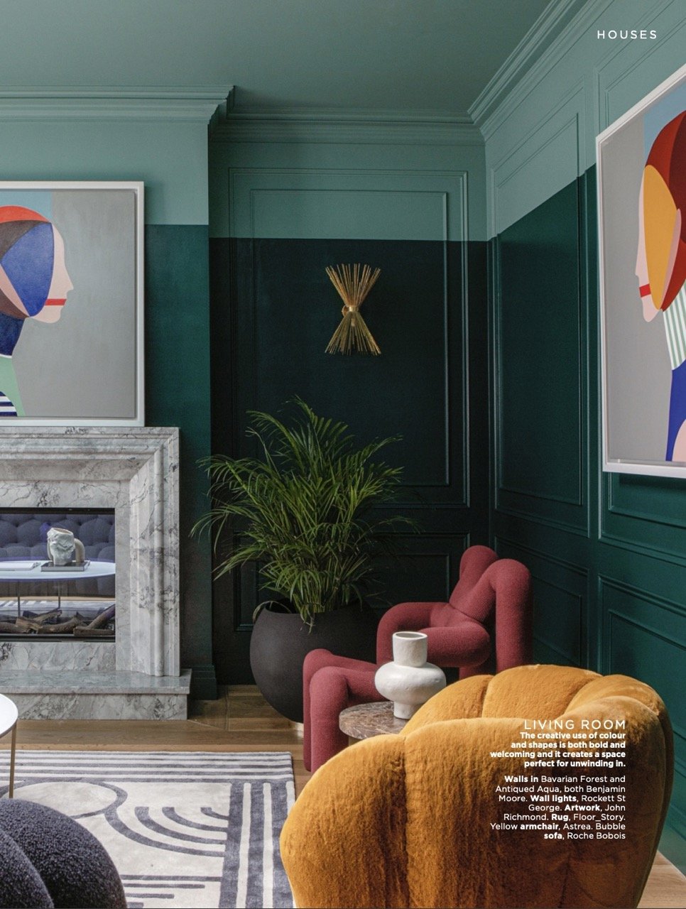 Interior of a living room with dark green walls, colorful abstract artwork, a marble fireplace, a large potted plant, a red upholstered armchair, a yellow armchair, and decorative vases.