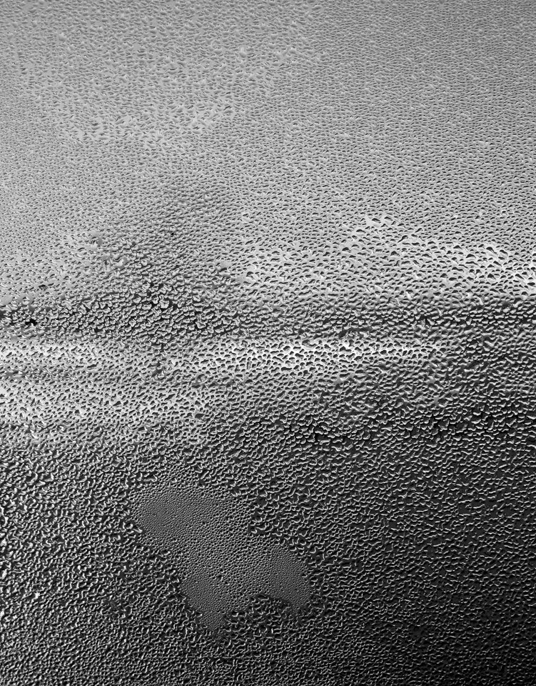 Close-up of a glass window with water droplets and condensation forming patterns.