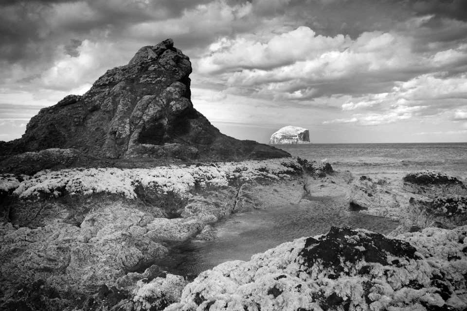 Rocky coastal landscape with large rock formations and an island in the distance under cloudy skies