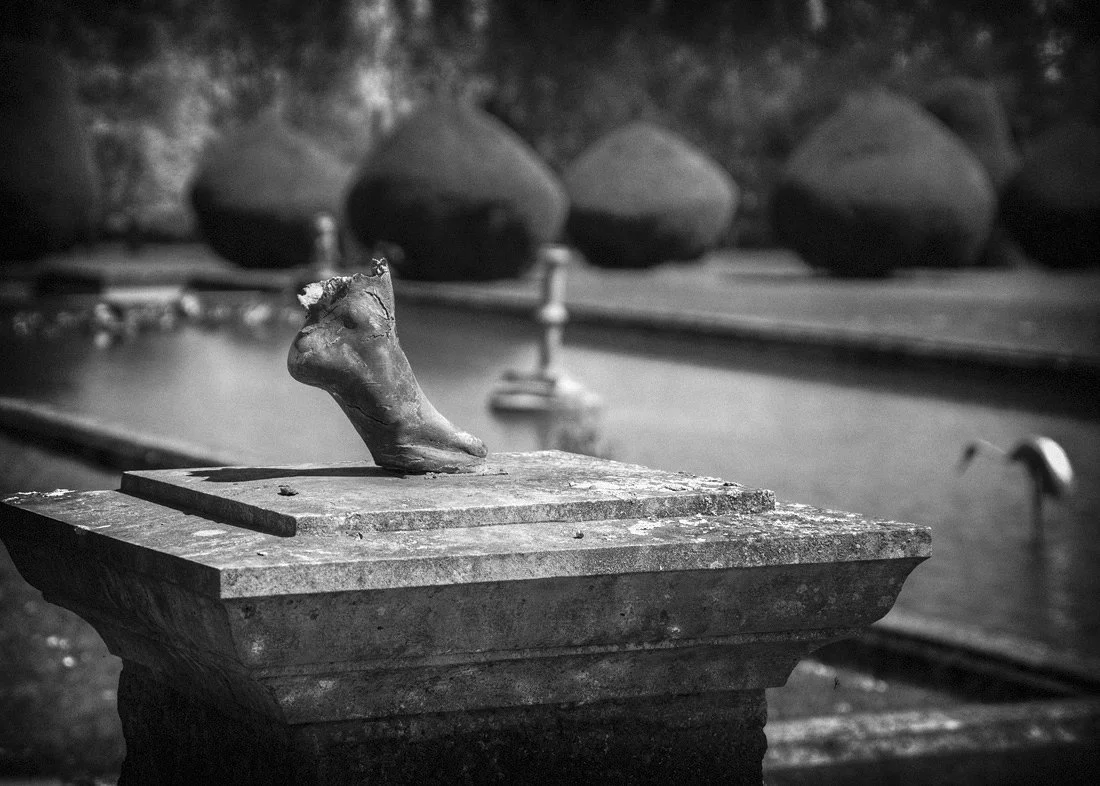 Black and white photo of a weathered sculpture of a foot on a pedestal.