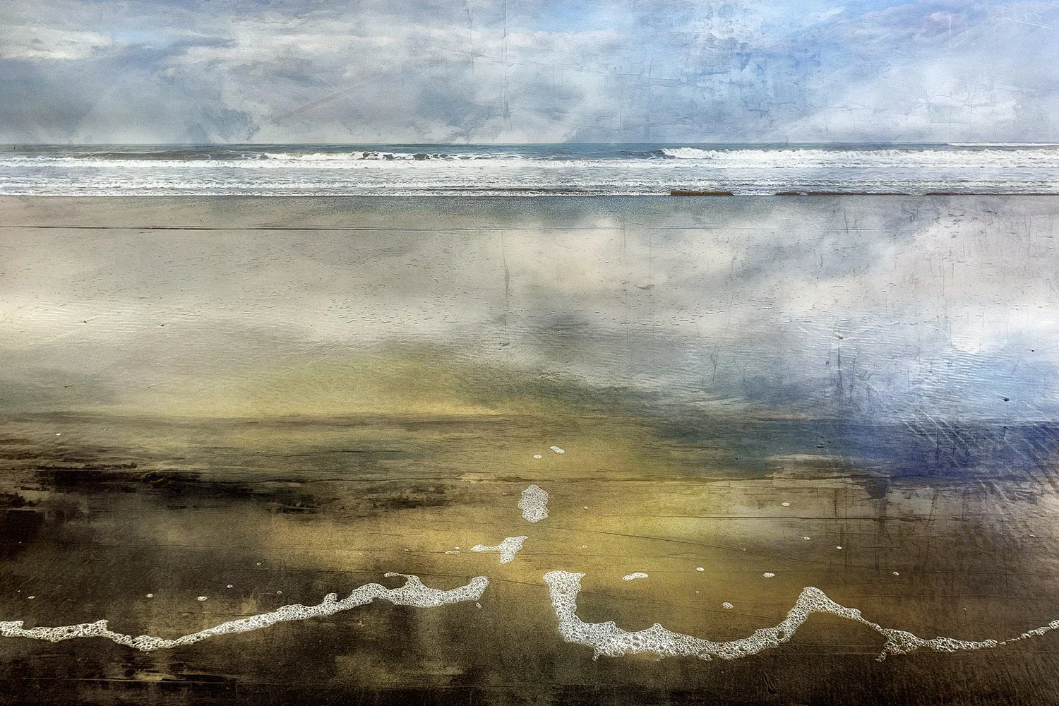 A beach scene with ocean waves, cloudy sky, and wet sand reflecting the sky, with foam from the waves at the shoreline.