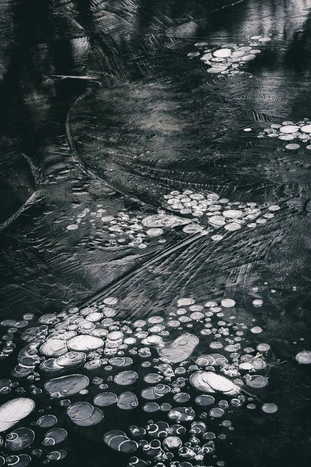 Close-up photo of icy water with bubbles and ice formations on the surface.
