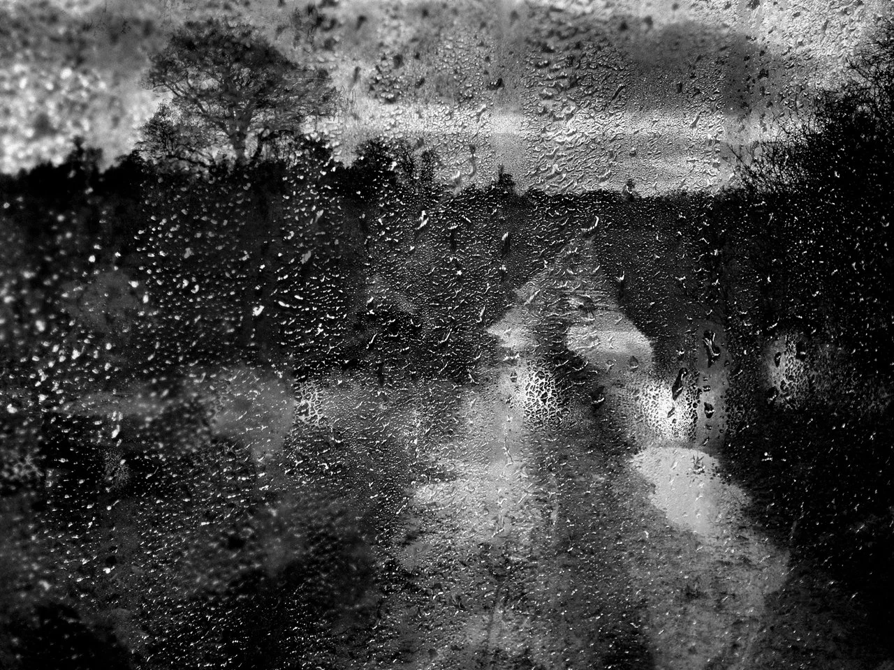 Rain-covered window with a blurred view of a road and trees outside