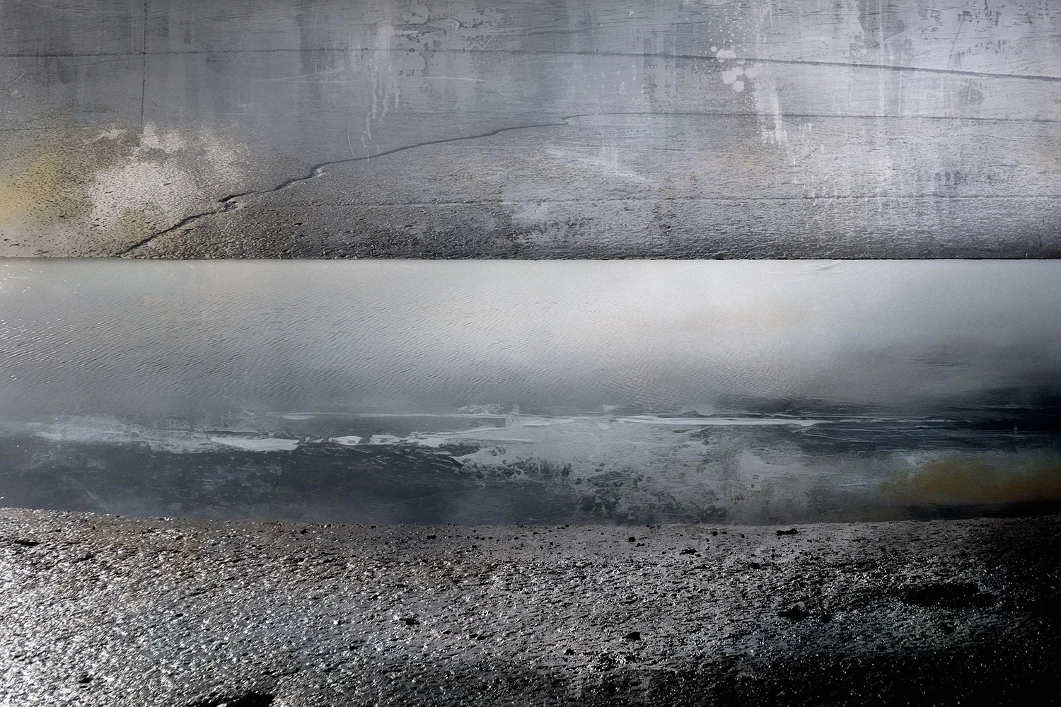 Close-up of a textured, matte black surface with a shiny, metallic, ridged strip running horizontally across the center, against a weathered, gray wooden background.