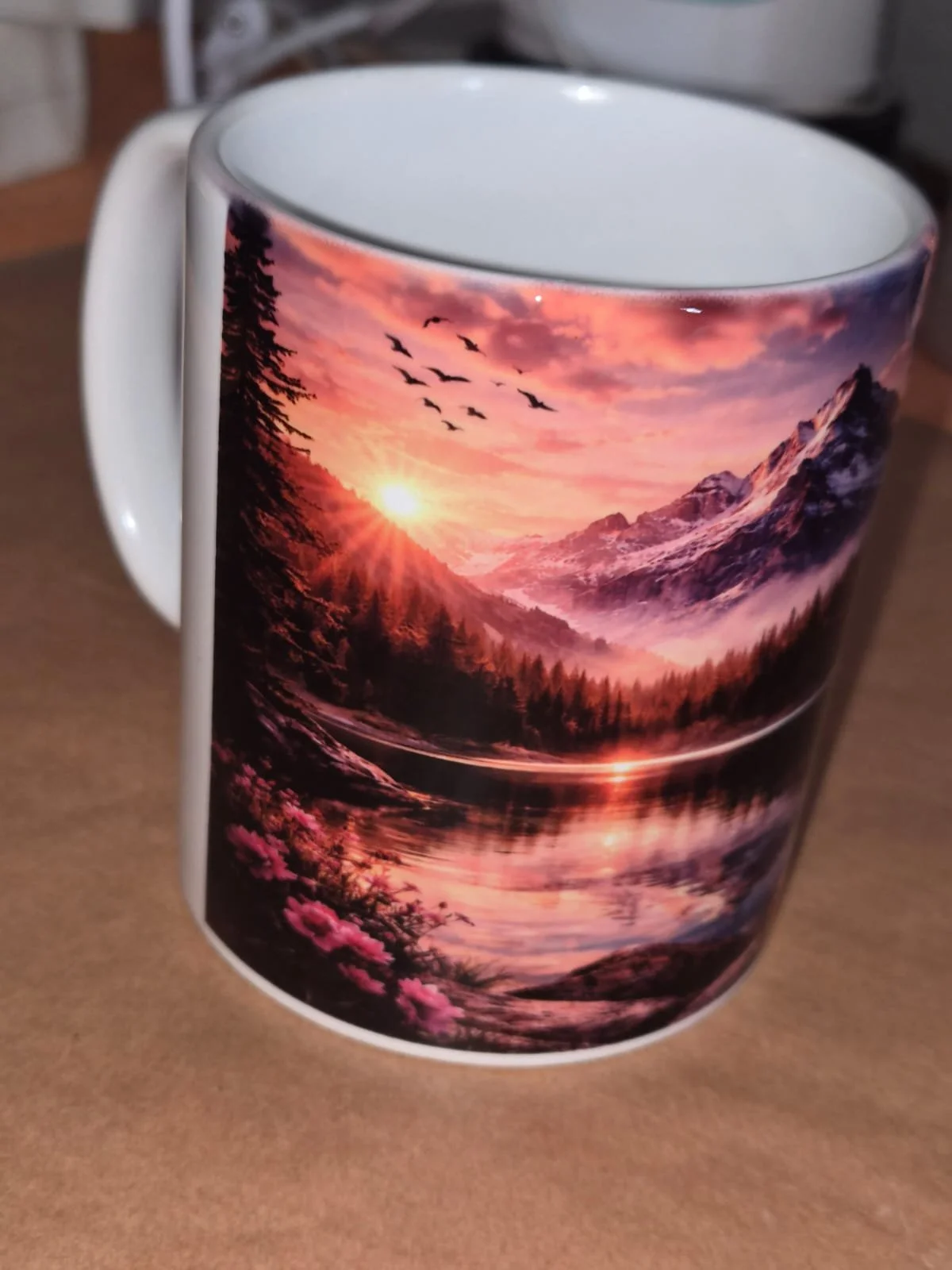 Tasse mit einem Landschaftsbild eines Sonnenuntergangs in den Bergen, mit Flüssen, Bäumen und Vögeln am Himmel.