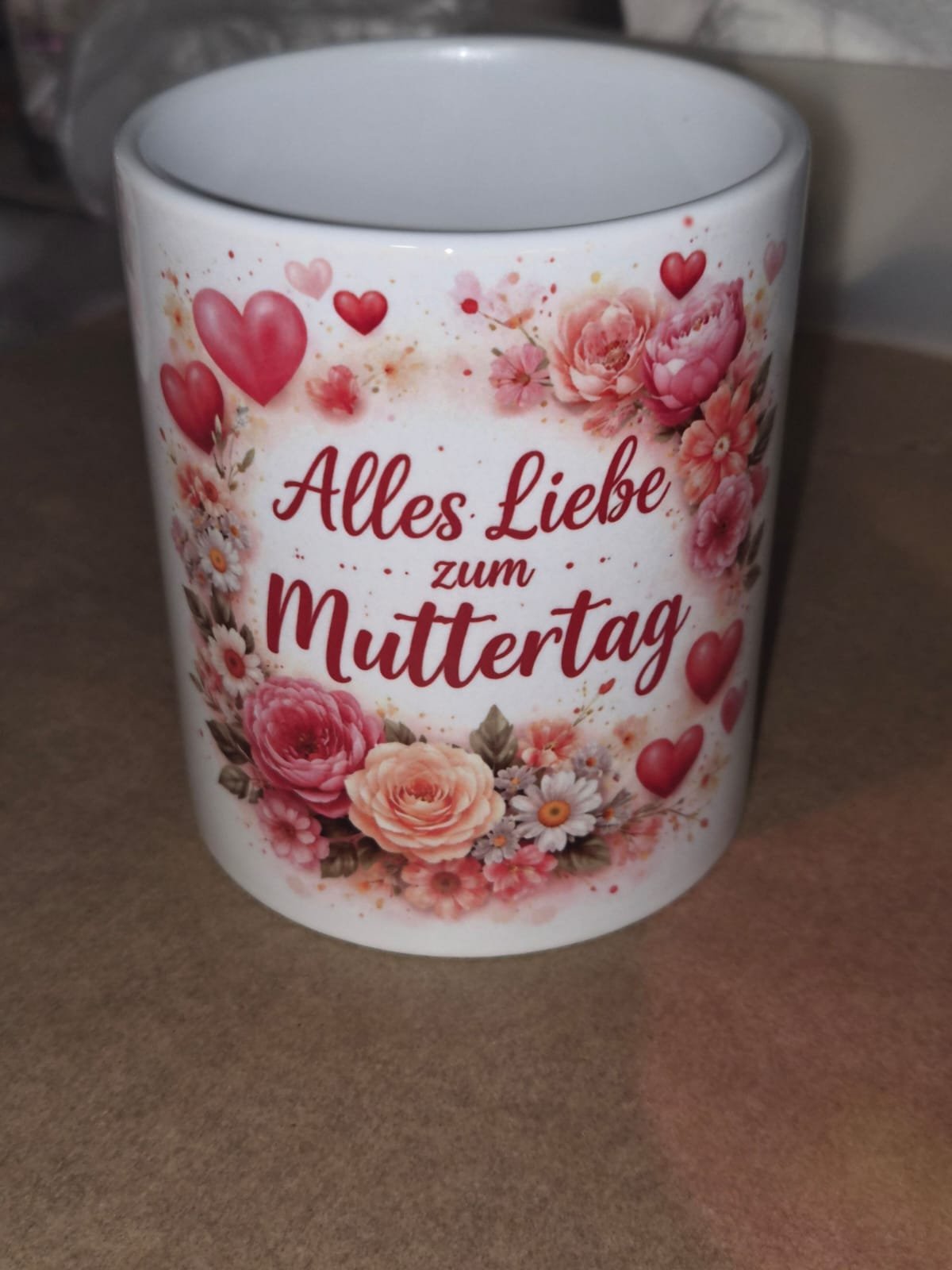 Tasse mit einem Blumen- und Herzmuster und der Aufschrift "Alles Liebe zum Muttertag" in roter Schrift.