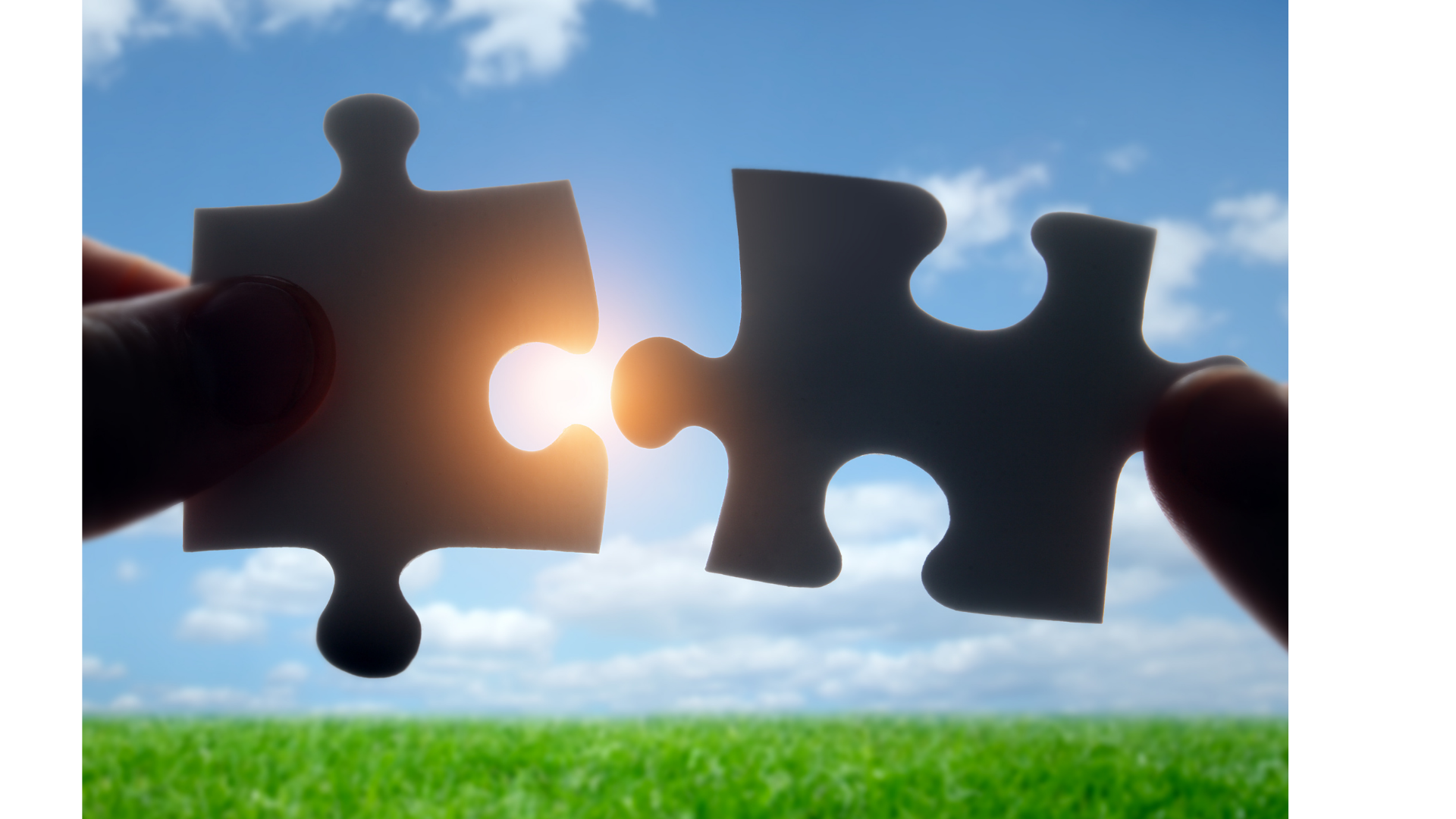 Two puzzle pieces being held up against the sky with clouds, fitting together with the sun shining through the gap.
