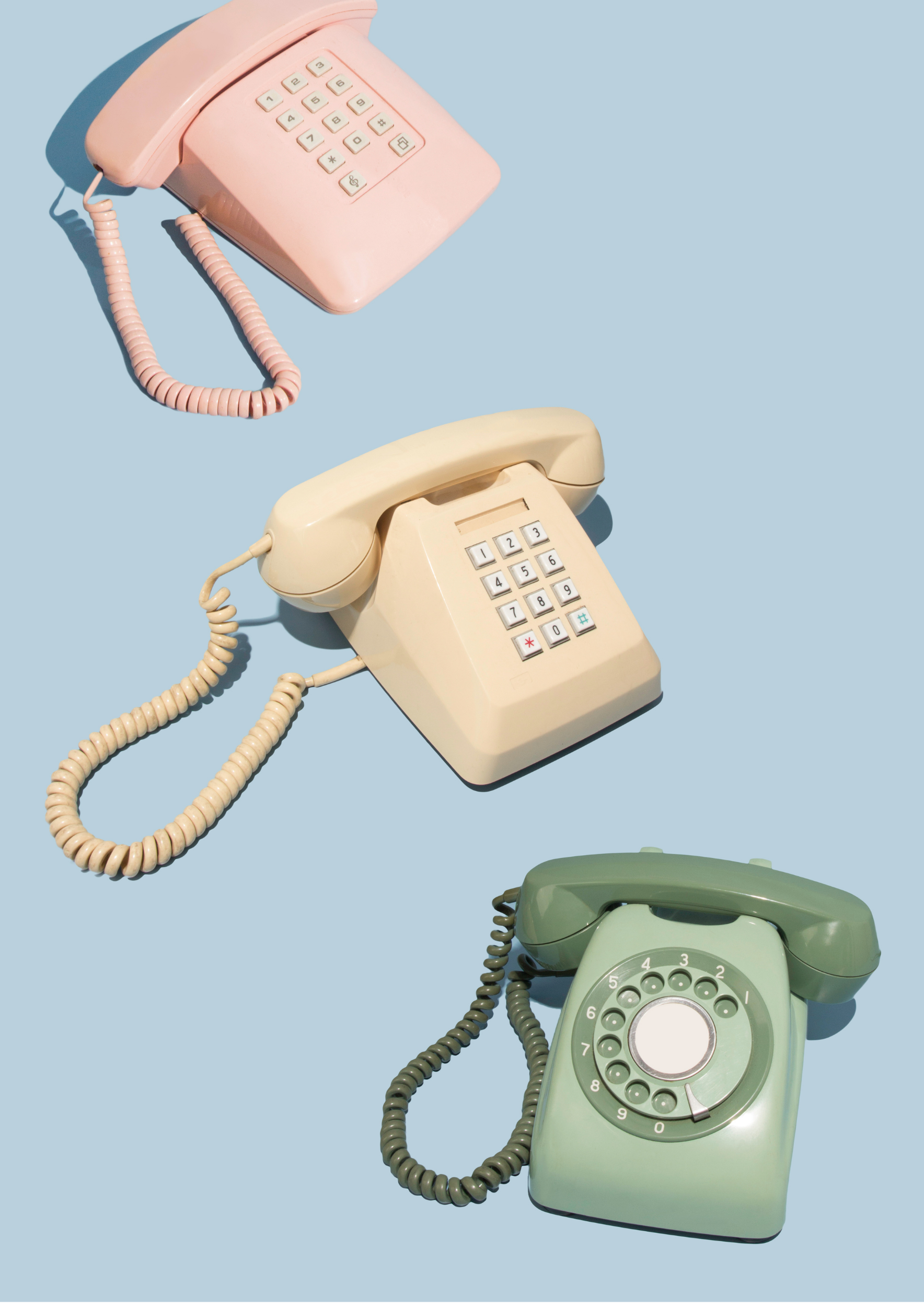 Three vintage rotary phones in pastel colors (pink, cream, and green) on a light blue background.