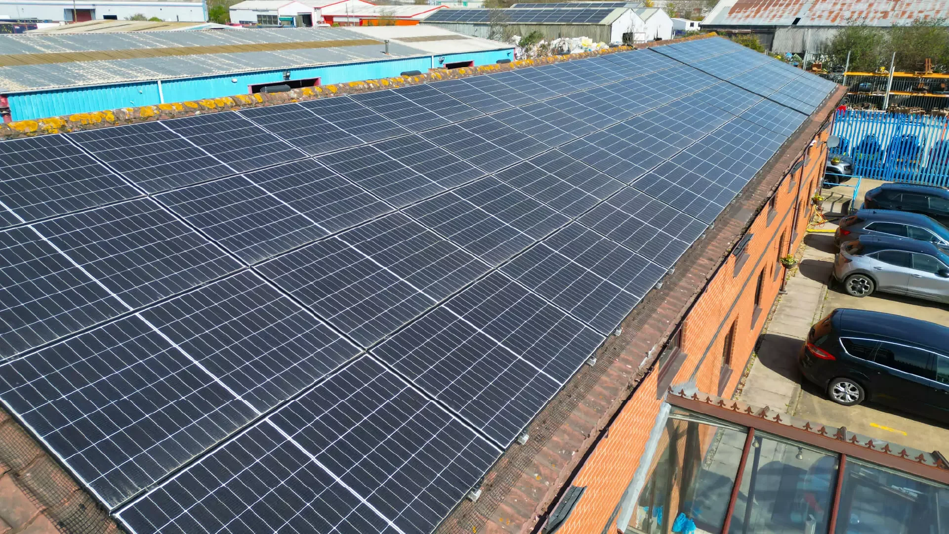 A rooftop covered with numerous solar panels beside a parking lot with five cars parked.
