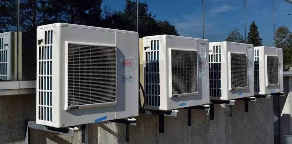 Four outdoor air conditioning units mounted on a concrete wall outside a building.