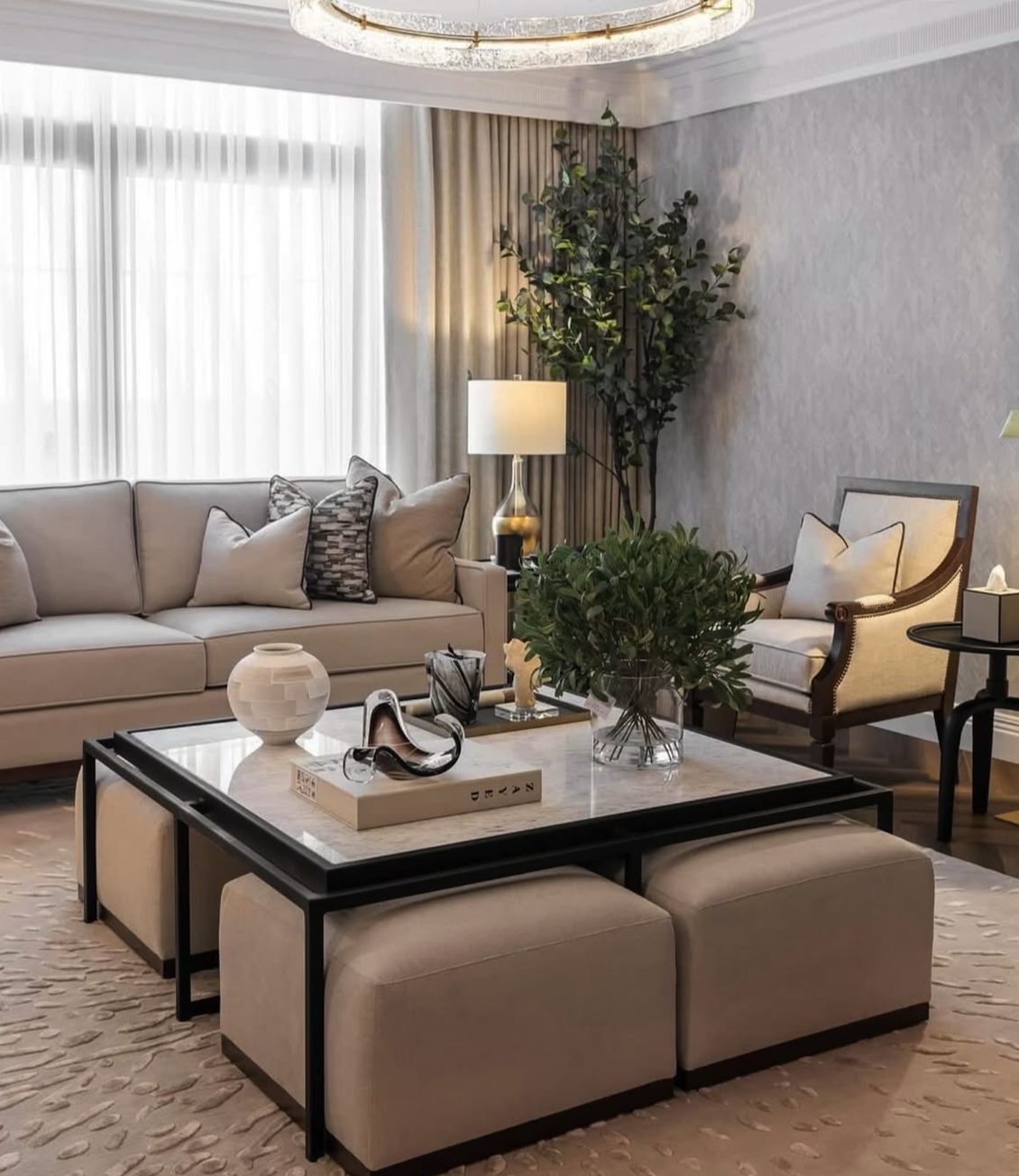Elegant living room with beige sofa, armchair, coffee table, indoor plants, and a large window with sheer curtains.
