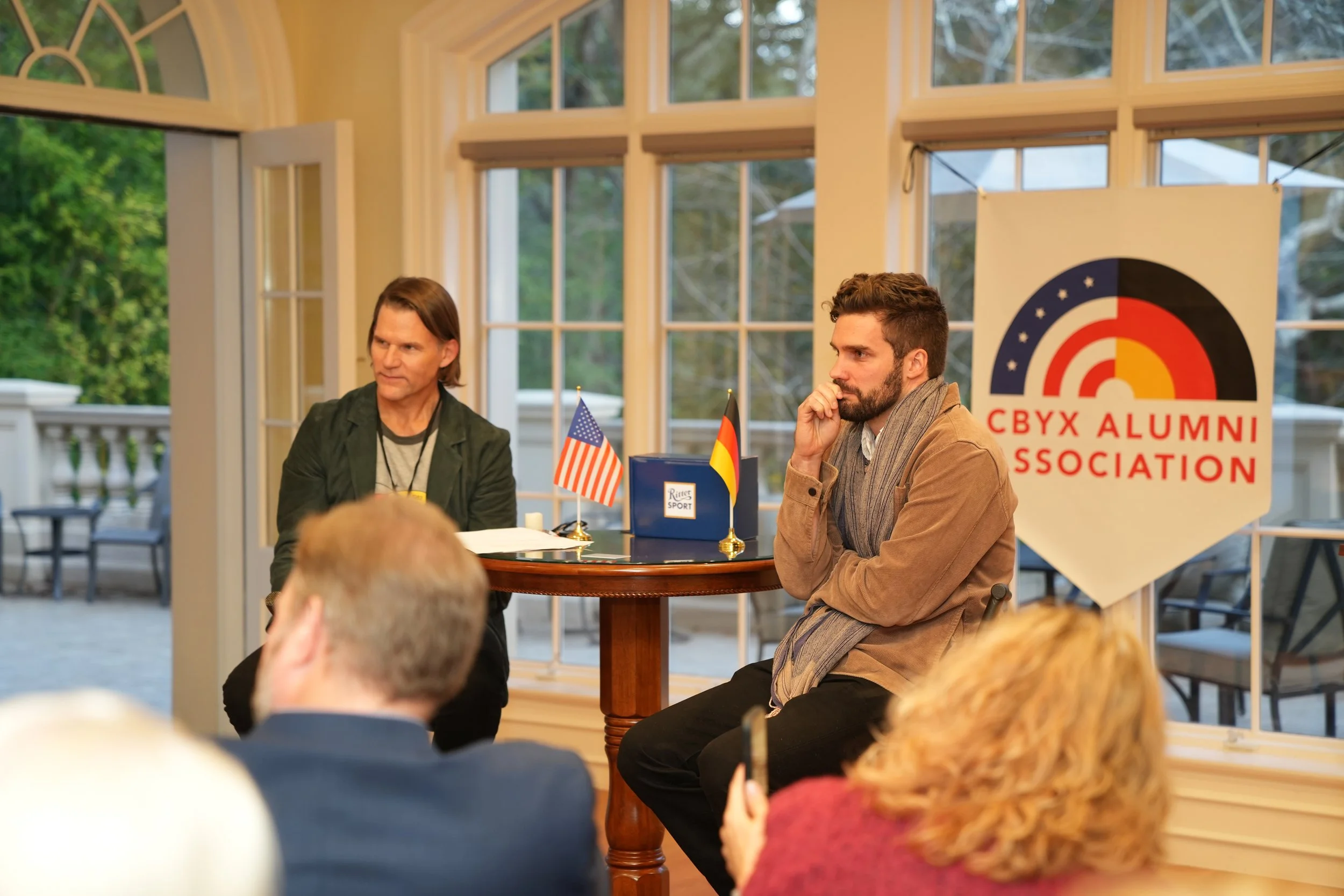 A panel discussion at a CBYX Alumni event with Jeremy Anderson, Philip Lindsley,  American and German flags, Ritter Sport. Halle House, 41st CBYX Alumni Year Celebration, 2025, Congress-Bundestag, State Department, Bard College