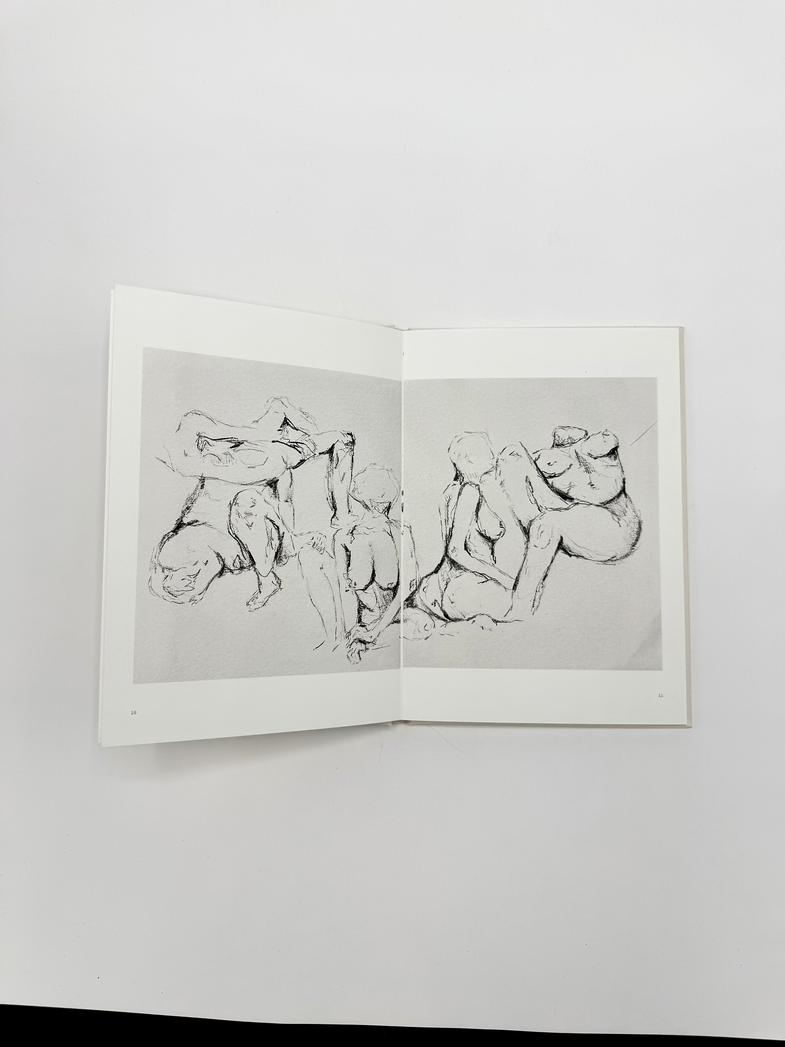 Open art book showing a black and white line drawing of figures with exaggerated proportions and organic forms, in a minimalist style, on a gray background.