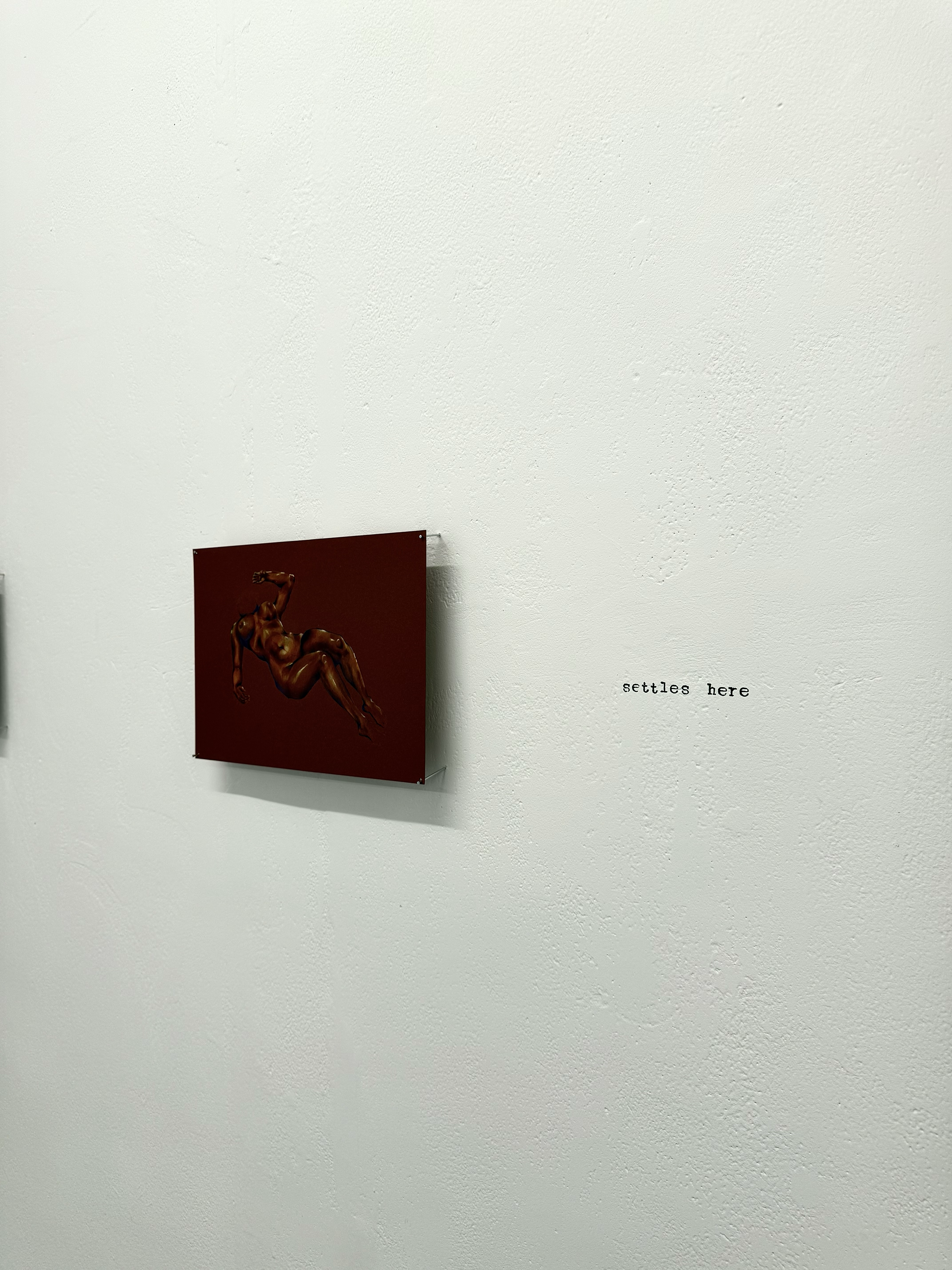 An art piece depicting a muscular, nude male figure in a reclining pose on a red background, hanging on a white wall with the words 'settles here' written on the wall next to it.