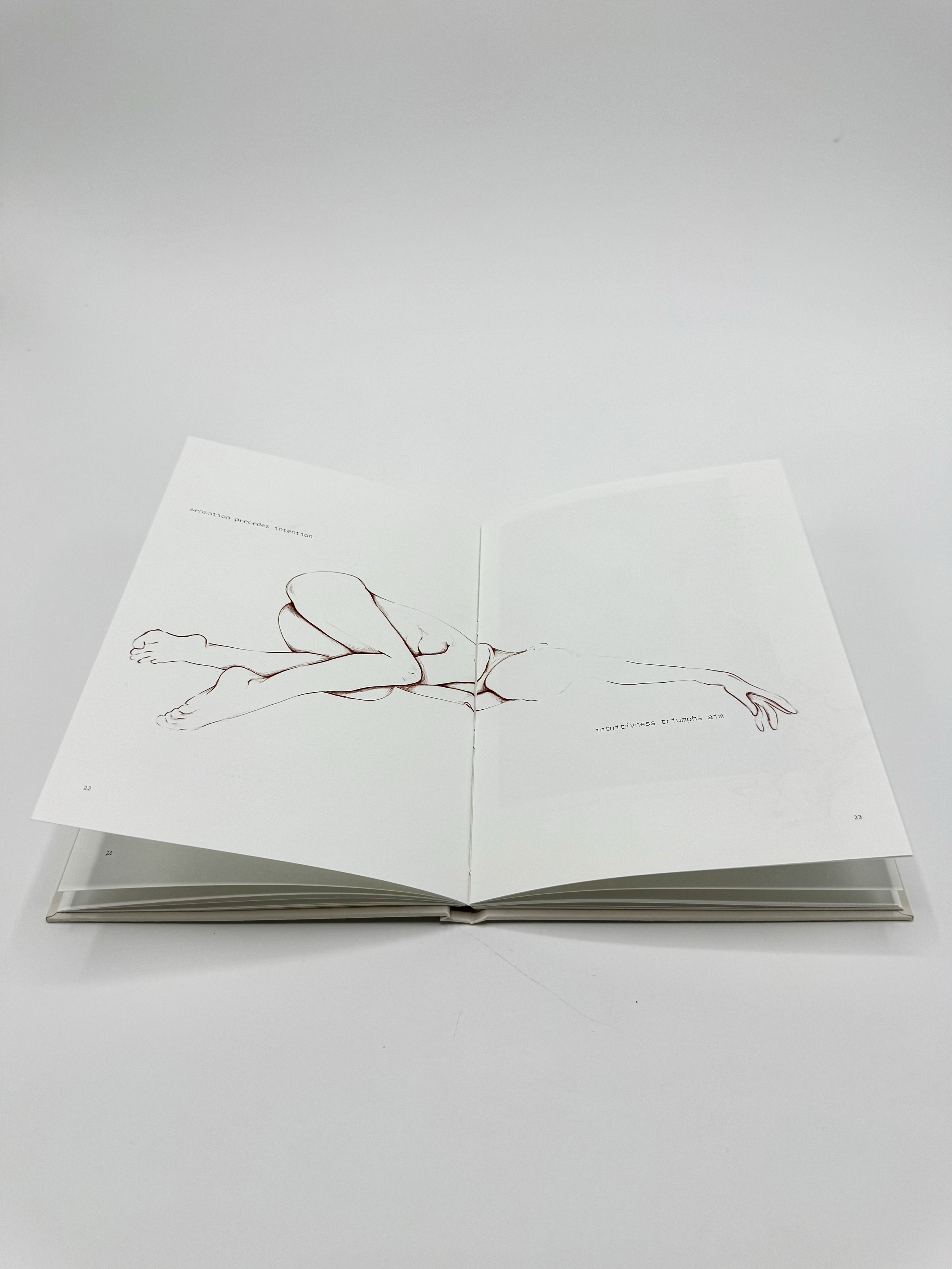 Open book with a line drawing of a human figure in a lying position on white pages, with text that reads "sensation precedes intention" and "intuitivness triumphs aim".