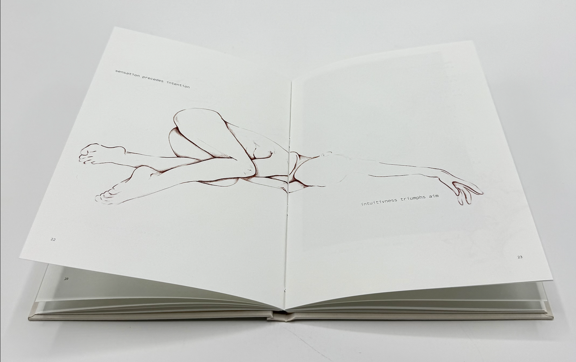 Open book with a minimalist line drawing of a reclining figure with legs bent and arms extended, and text that reads "sensation precedes intention" on the left page and "intuitiveness triumphs aim" on the right page.