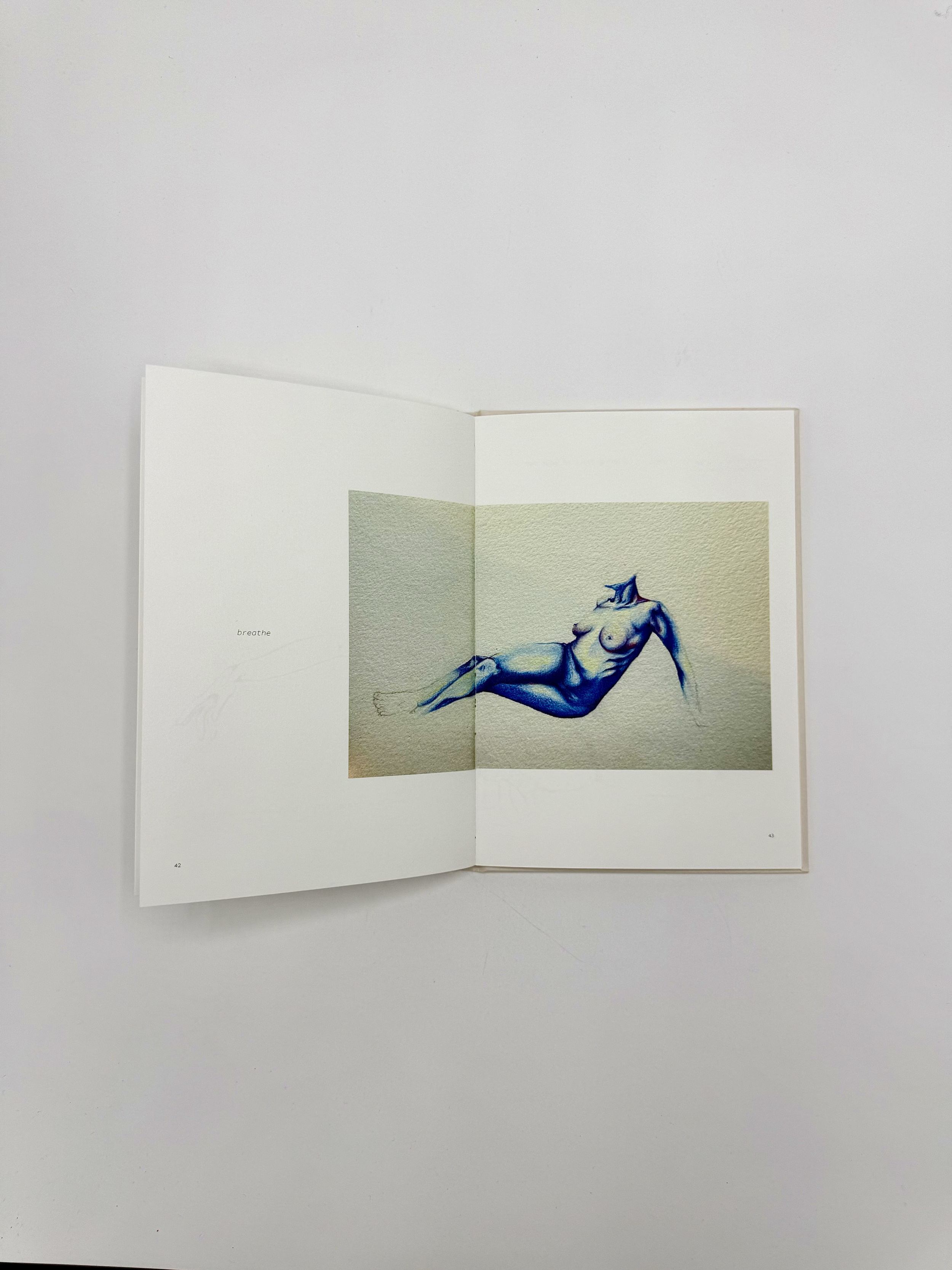 Open art book showing a watercolor painting of a reclining female nude with blue tones, with minimal text visible.