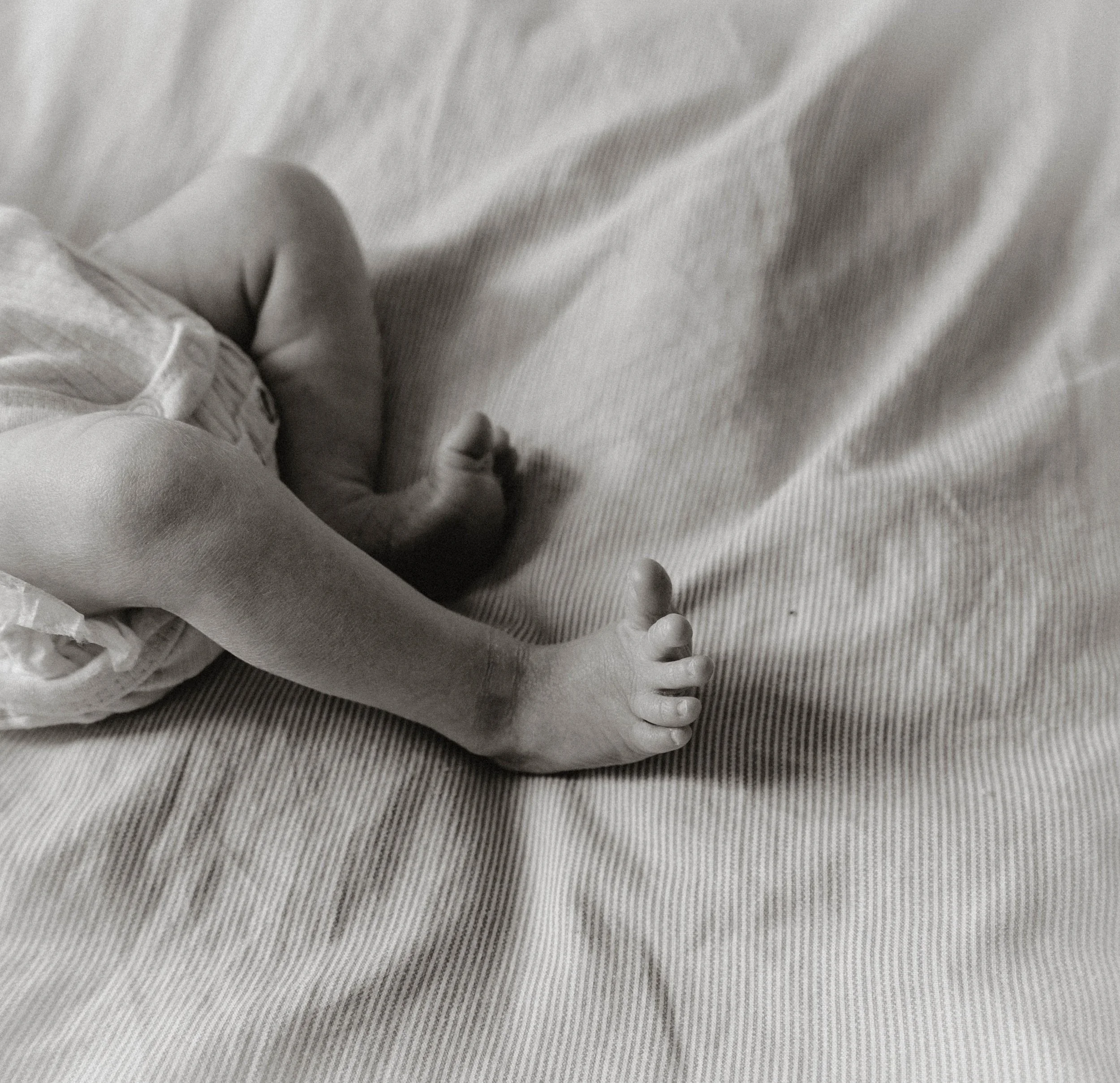 Close-up of a baby's hand resting on a fabric surface, with the baby wearing a long-sleeve garment.