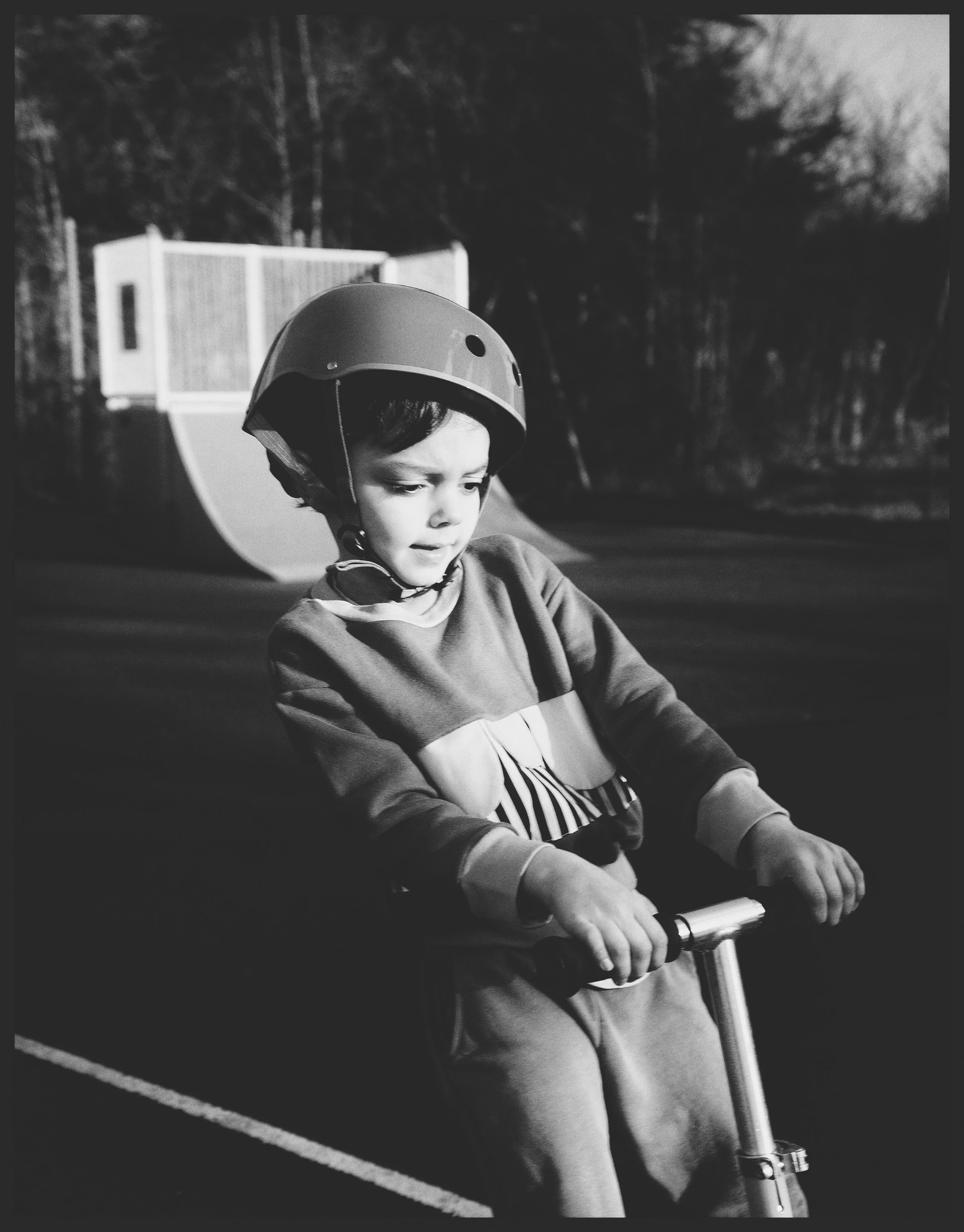 A young boy wearing a helmet and riding a scooter outdoors during daytime.