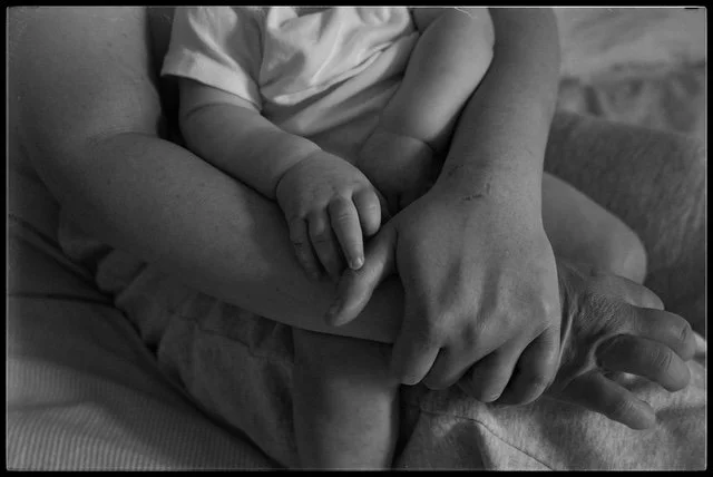Close-up of a child's hand holding an adult's hand, both resting on a person's lap.