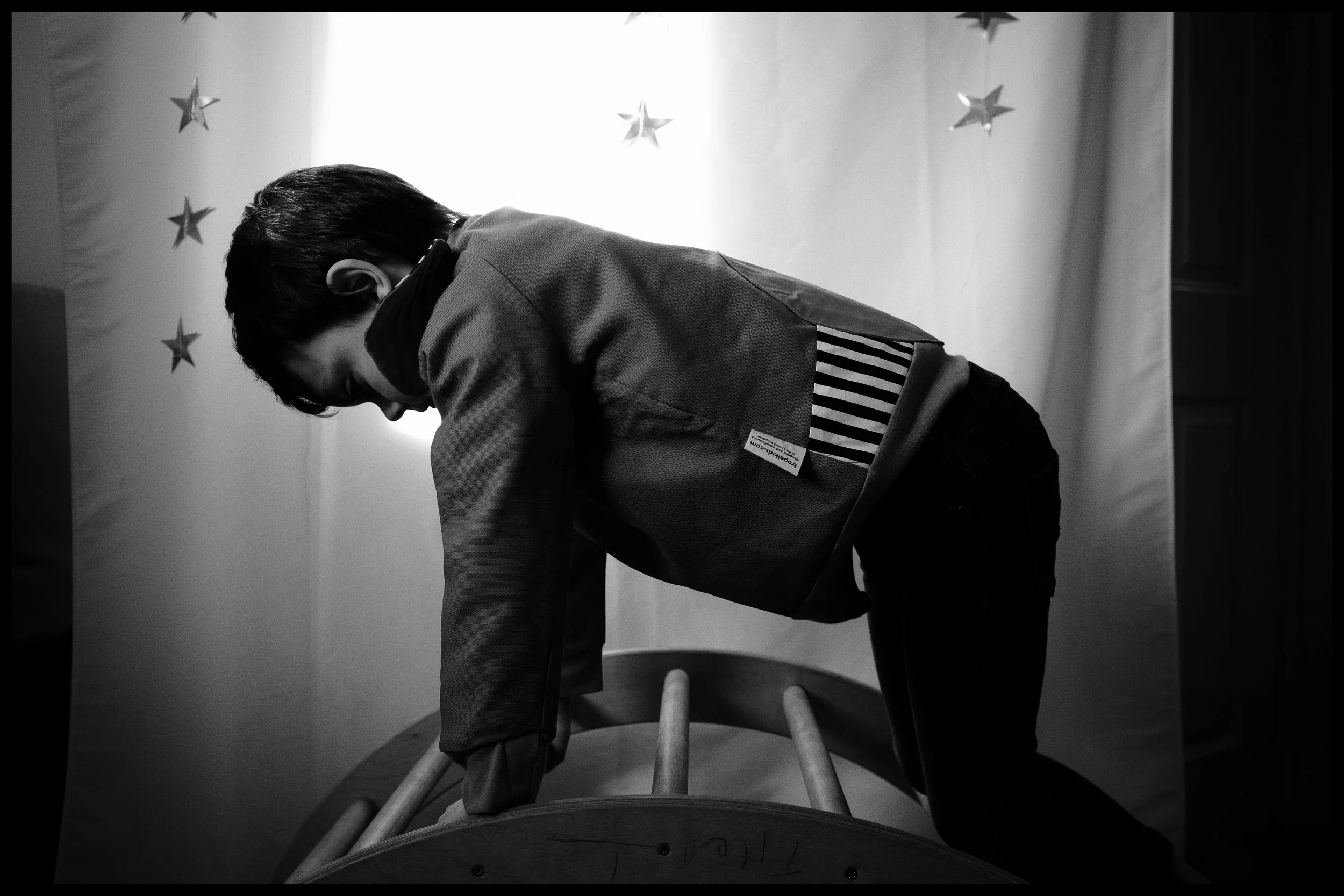 A person leaning forward on a wooden chair, face turned downward, with a background decorated with stars.