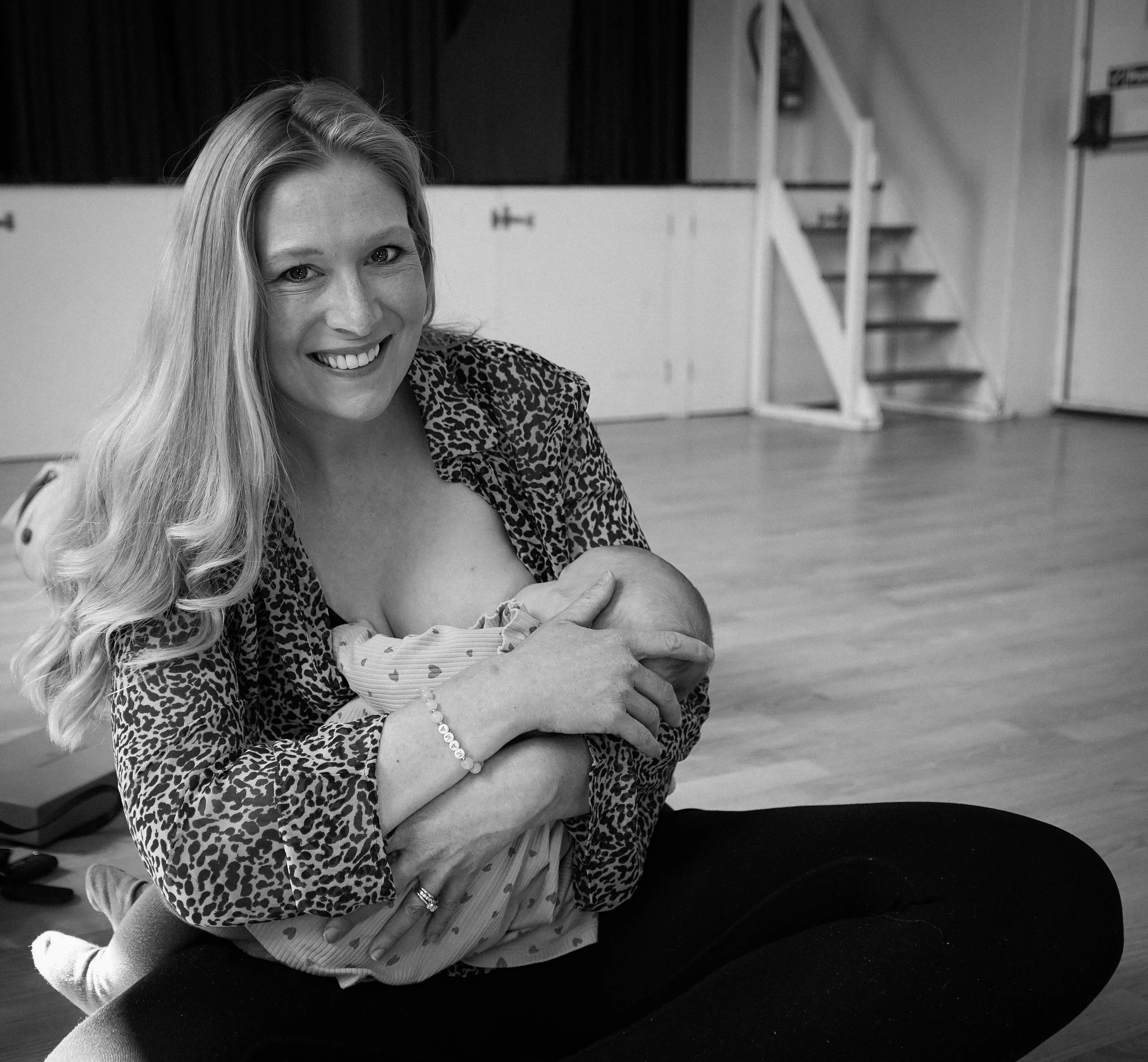 Smiling woman with long blonde hair wearing animal print top, holding a tearful baby.