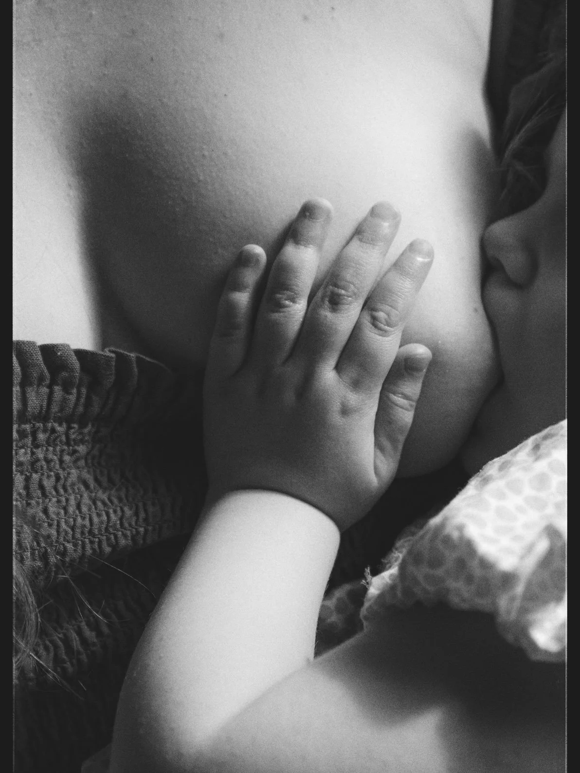 A black-and-white photograph of a young child kissing the bare chest of an adult, with a hand resting on the adult's chest. The child's face is turned to the side, and the adult's face is not visible.