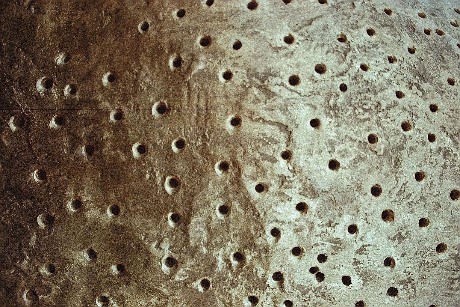 Close-up view of a weathered surface with numerous small, round holes arranged in a pattern.