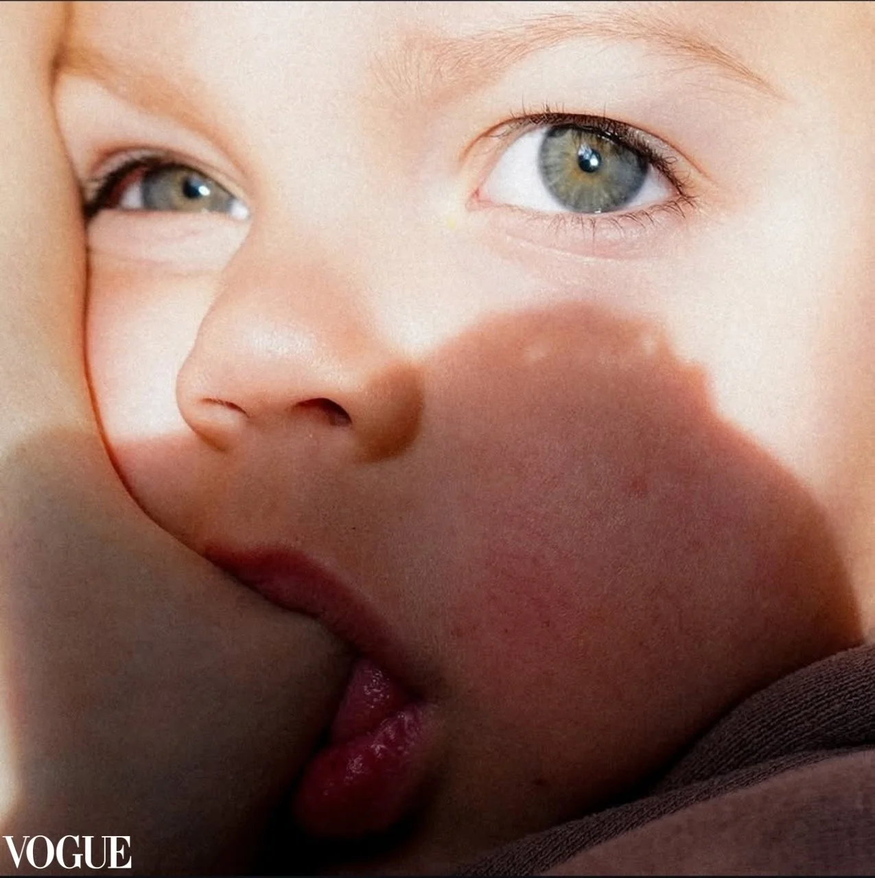 Close-up of a person's face with blue eyes, focusing on the eyes and nose, with a shadow of a finger on the face.