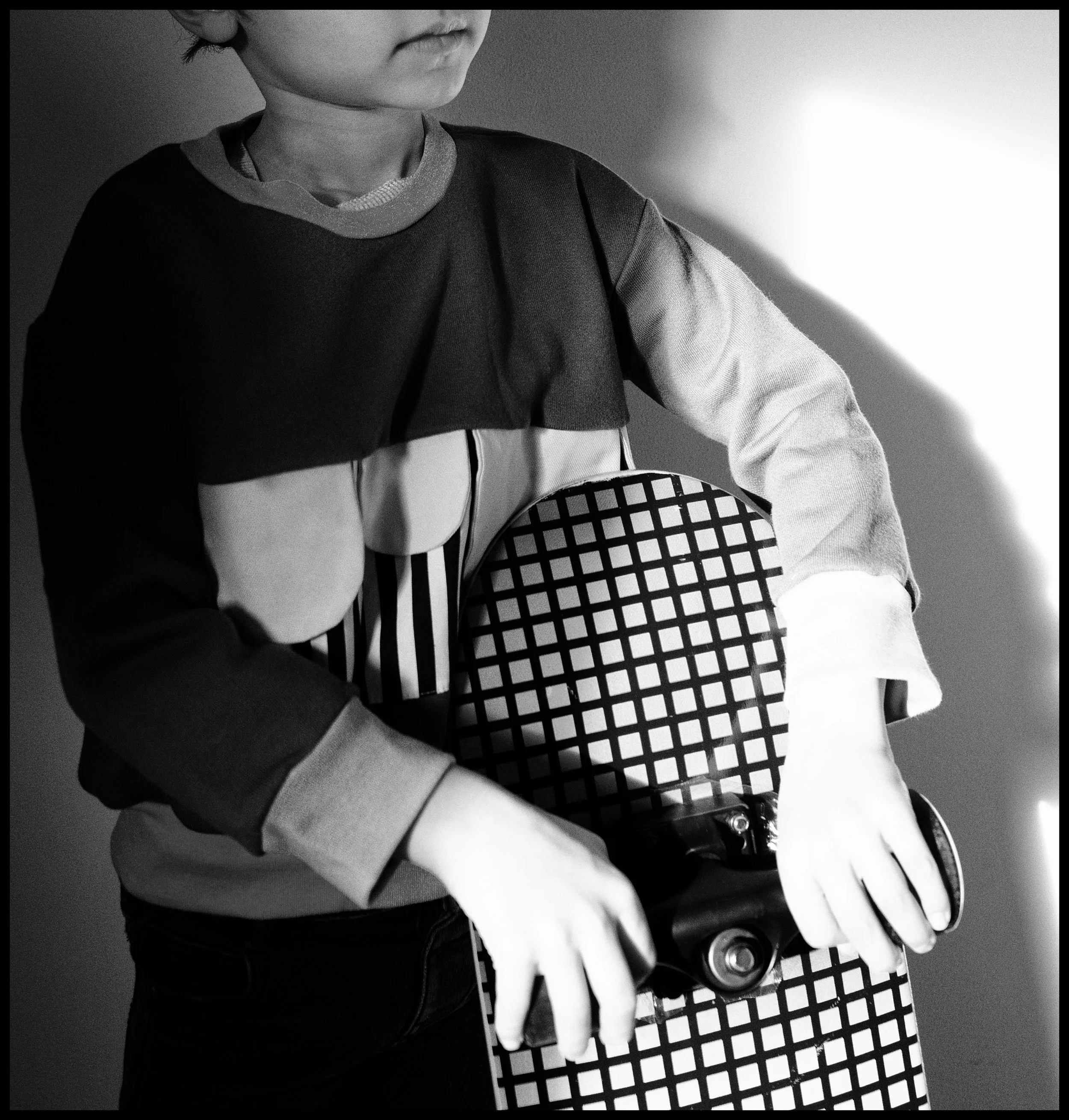 Close-up of a child in a long-sleeve shirt holding a tennis racket with a checkered pattern, black and white.