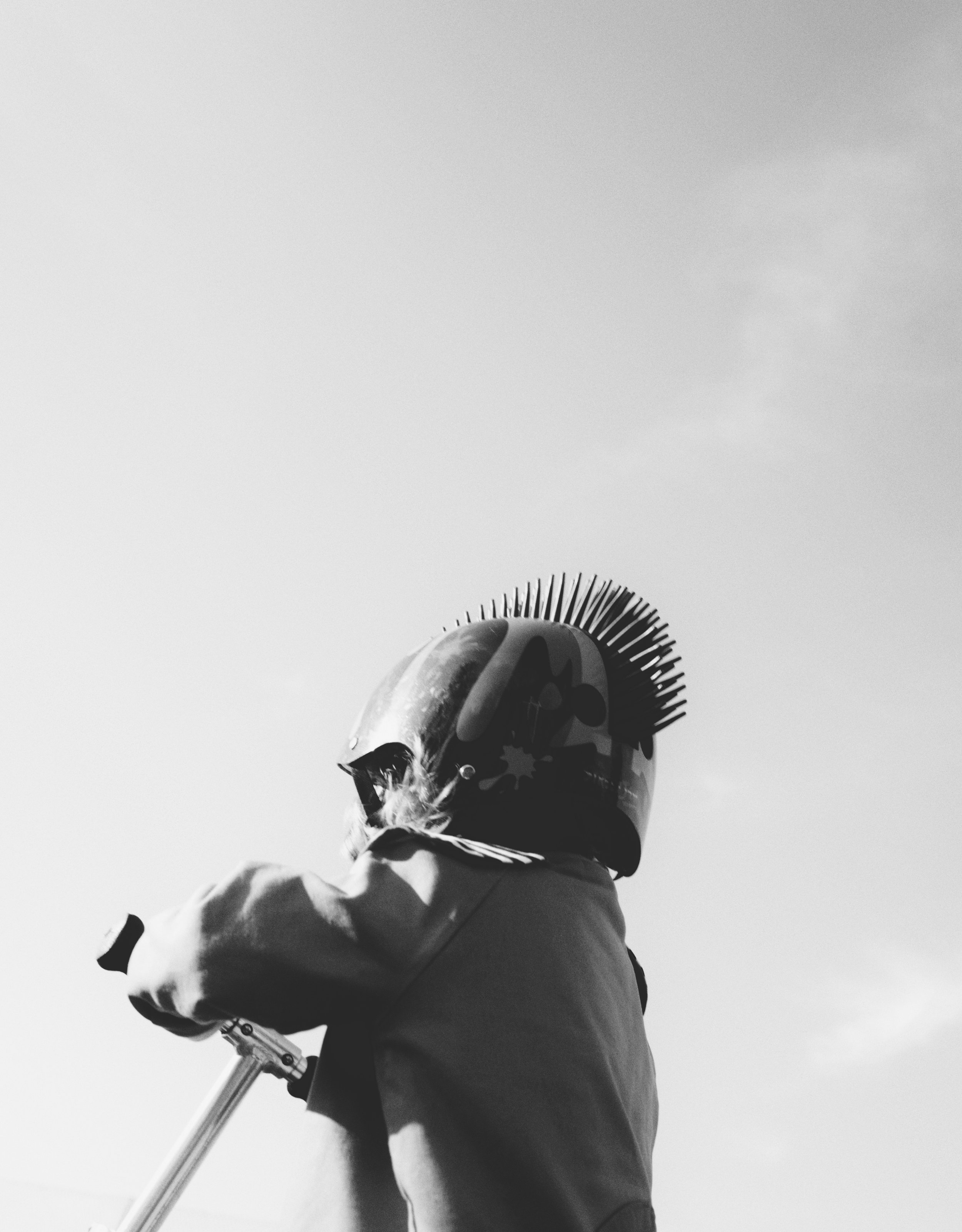 A person wearing a helmet, scarf, and coat standing outdoors with a bicycle, viewed from a low angle with the sky in the background.