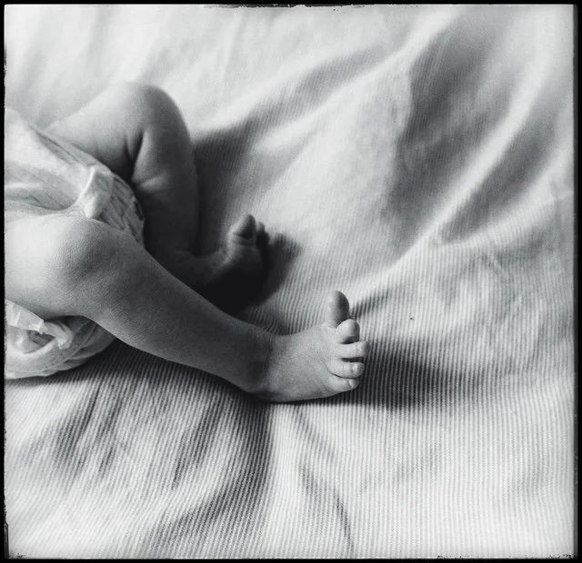 Close-up of a baby's legs and feet lying on a textured surface, with the baby wearing a diaper.