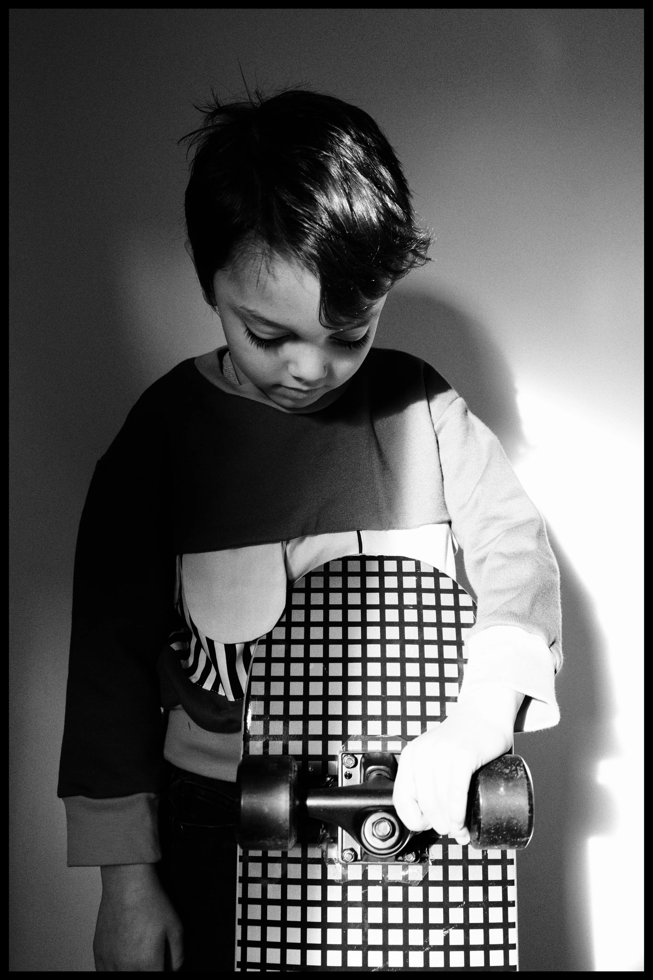 A young child with short dark hair riding a skateboard, wearing a jacket with a graphic design on the front, in black and white.