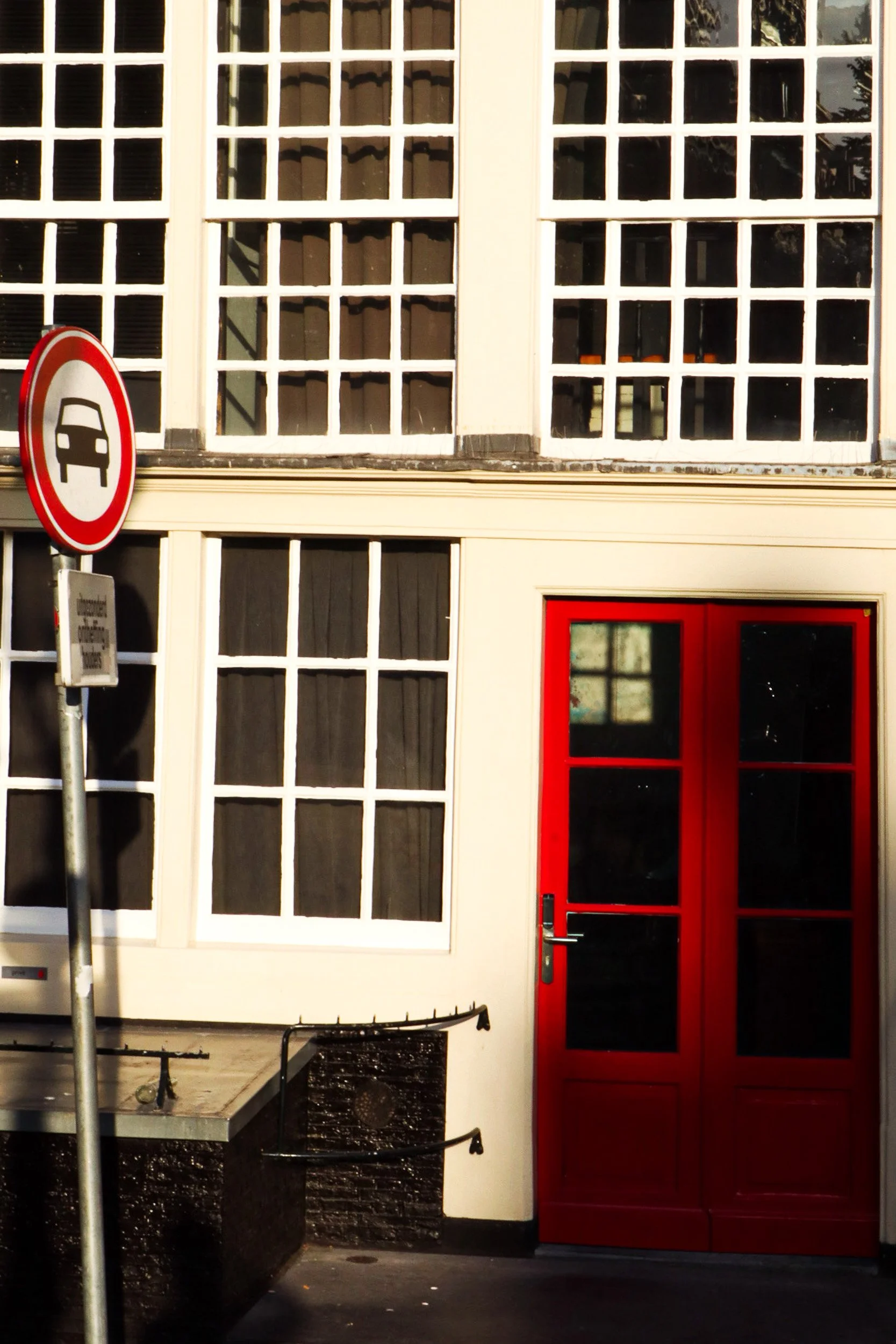 Amsterdam building facade with red door and large windows. Street photography by Isabel Hachmann-Peralt.
