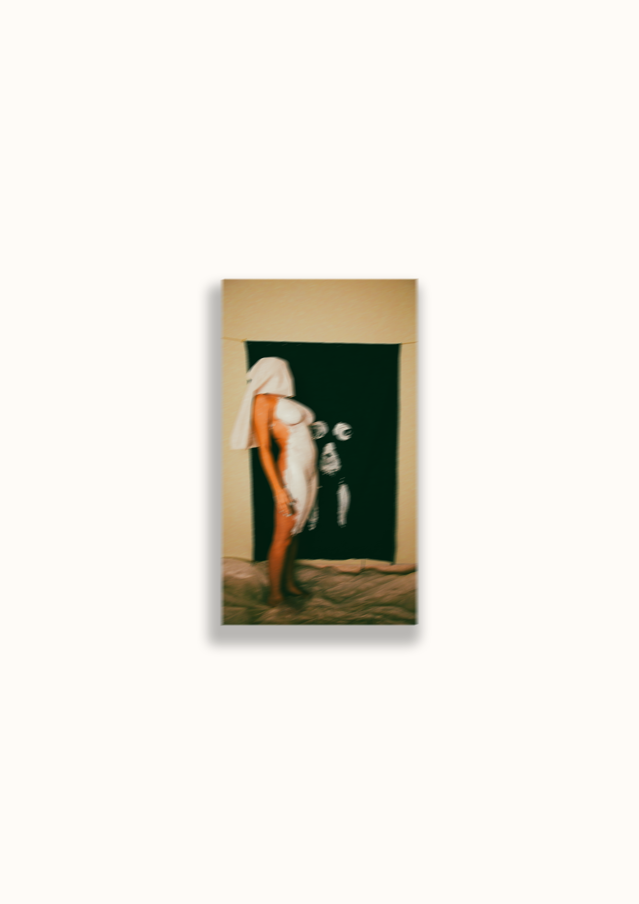 A woman with long blonde hair, wearing a white top and orange pants, standing in front of a dark background with white symbols on it, on a tan carpeted floor.