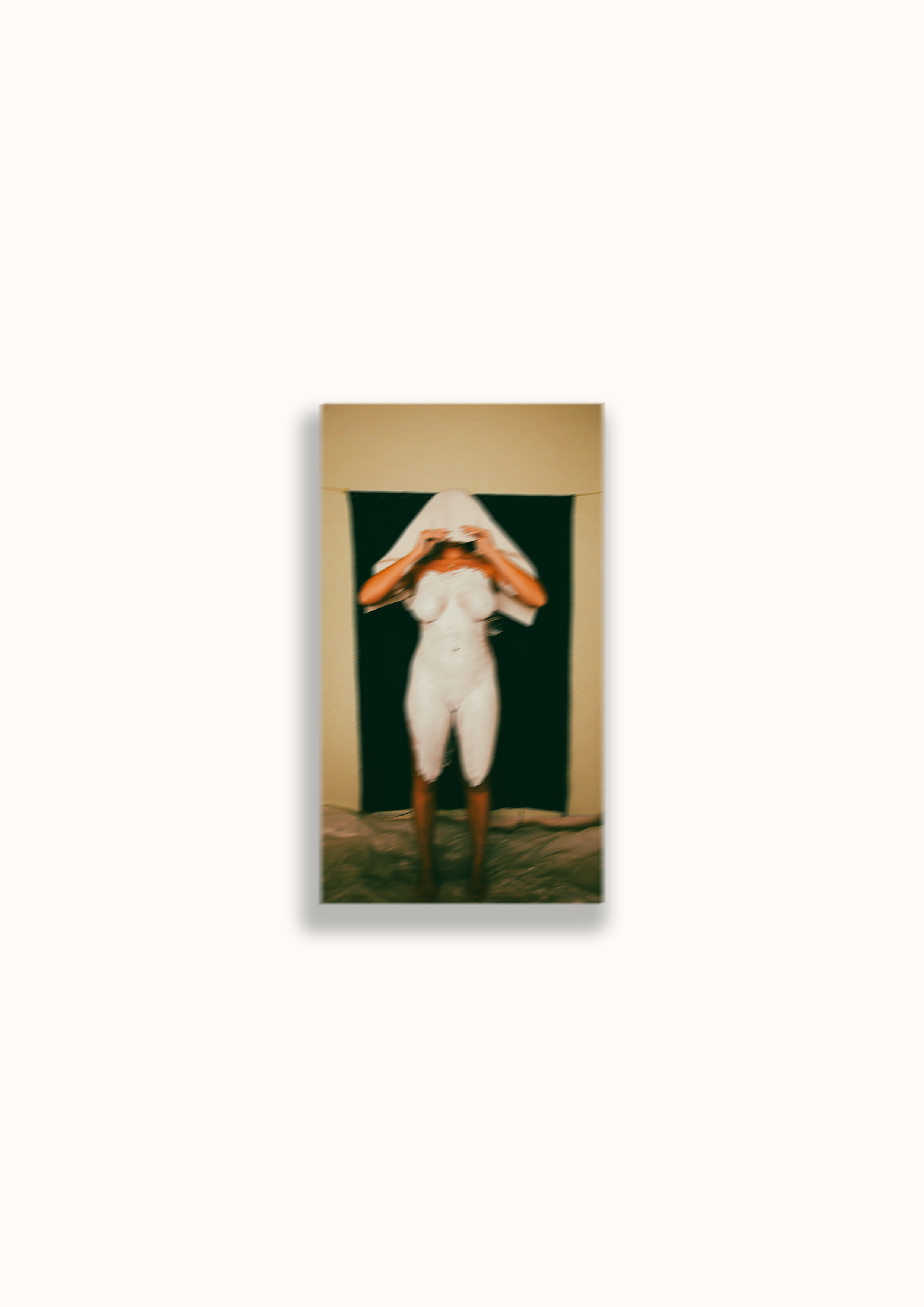 A woman standing in front of a mirror, taking a photo with her phone, wearing a white dress with a towel covering her head.