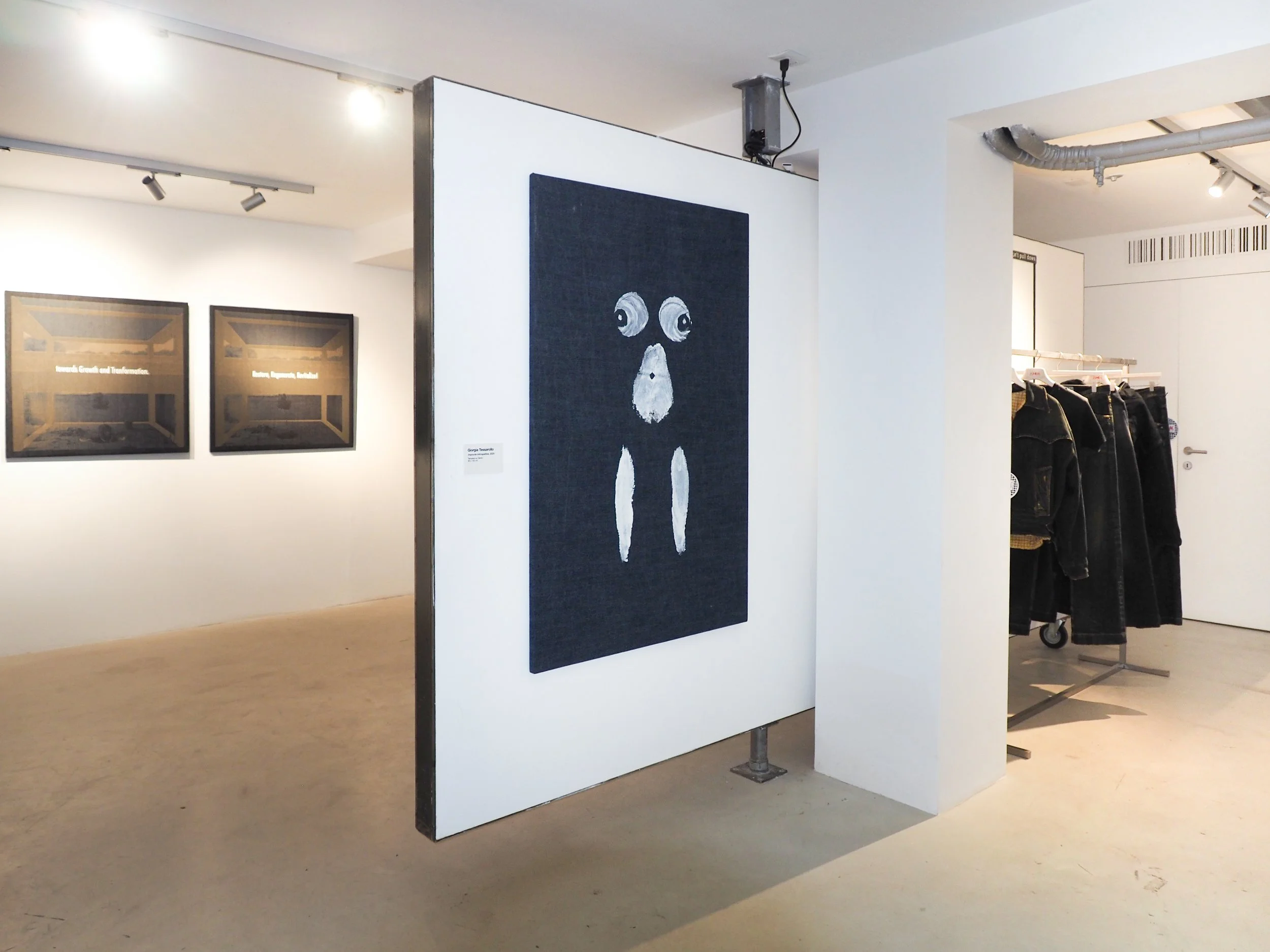 An art gallery with artworks on the white walls and a black portrait with white eyes and a white beard or mustache on display.