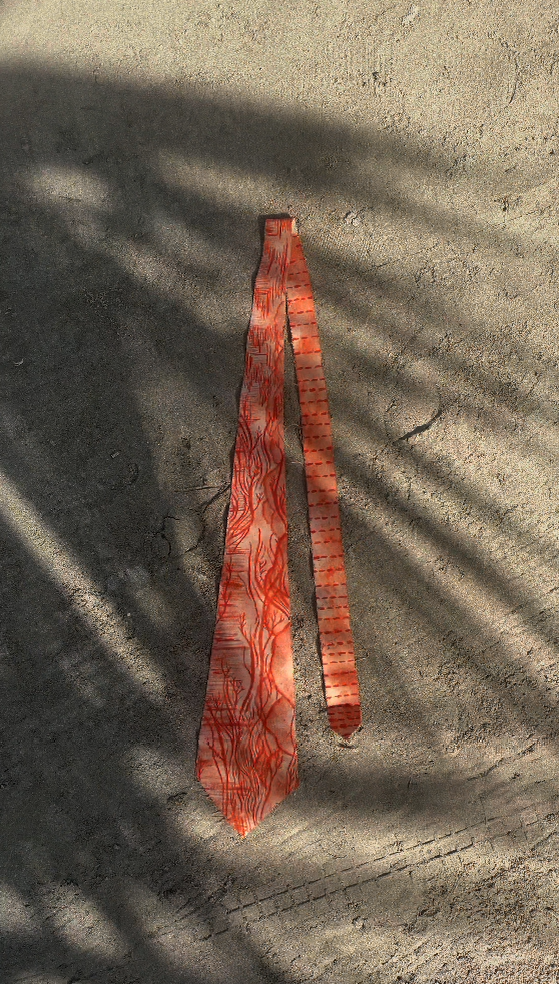Two fabric straps with orange and red patterns lying on a concrete ground, casting shadows.
