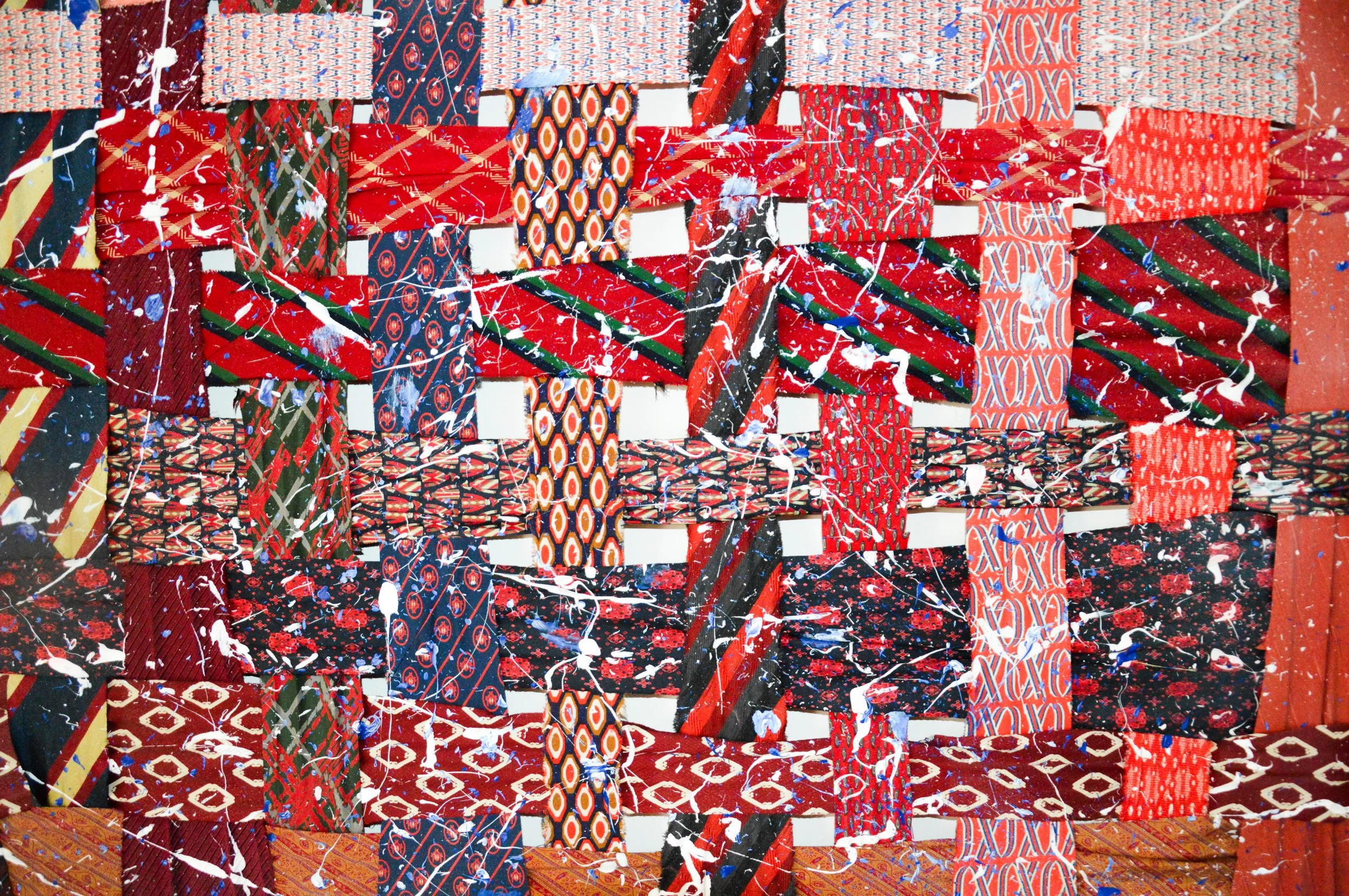 Close-up of a woven canvas with a collage of various patterned and colored ties, decorated with white and blue paint splatters.