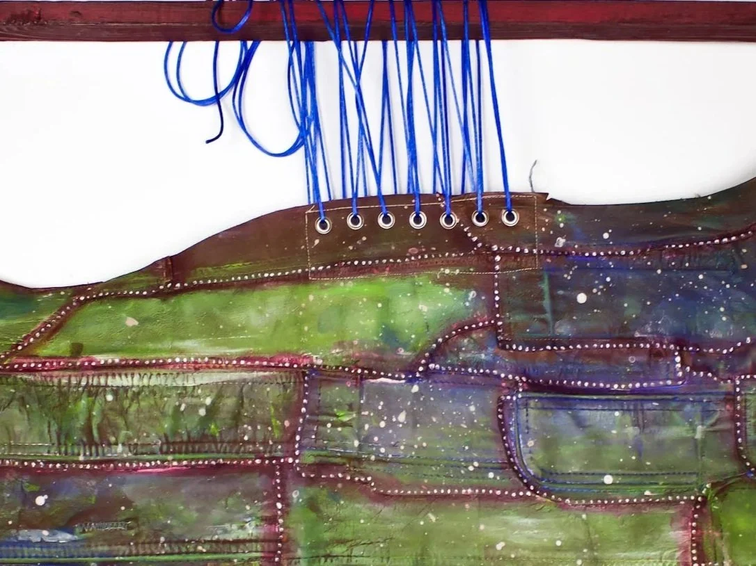 Close-up of a colorful abstract painting with stitched outlines and blue hanging strings at the top.