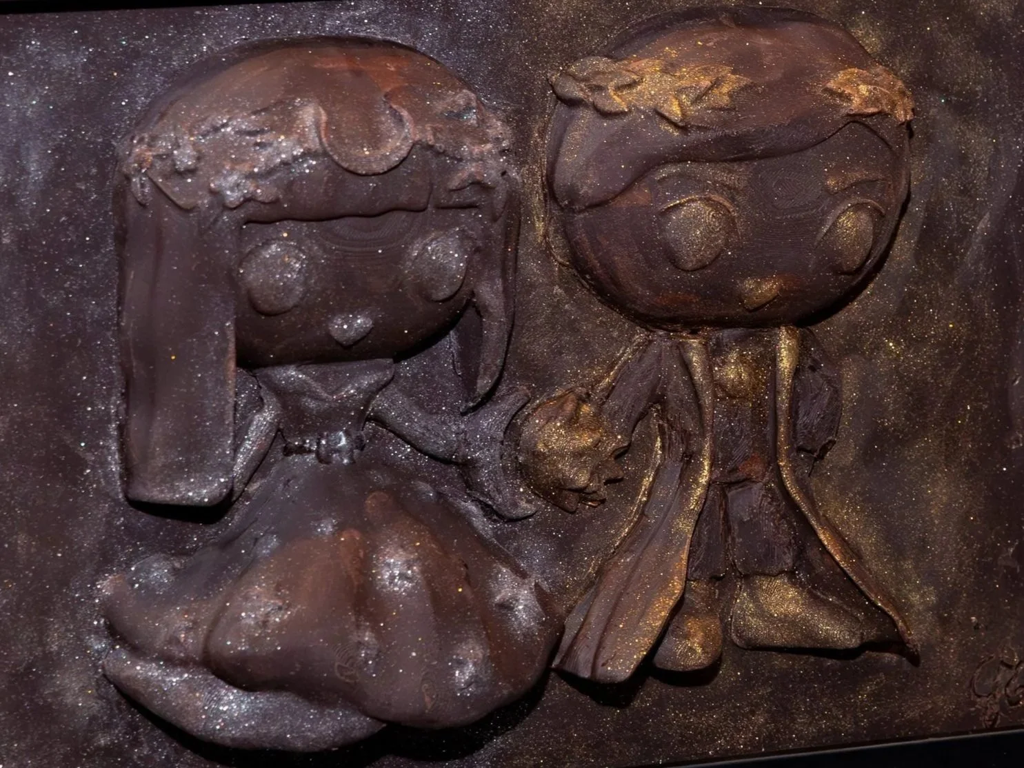 A chocolate relief sculpture of a girl and a doll with glitter accents.