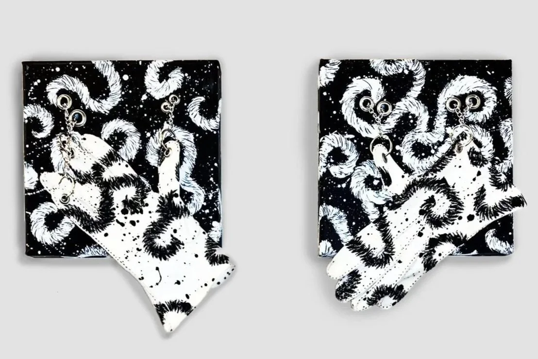 Pair of black and white abstract art pieces with patterns resembling swirling lines, dots, and pig-shaped prints, each with a white glove with similar pattern placed in front.