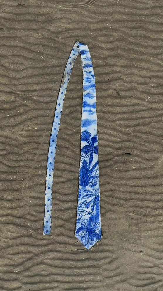 A blue and white patterned scarf lying on sandy ground.